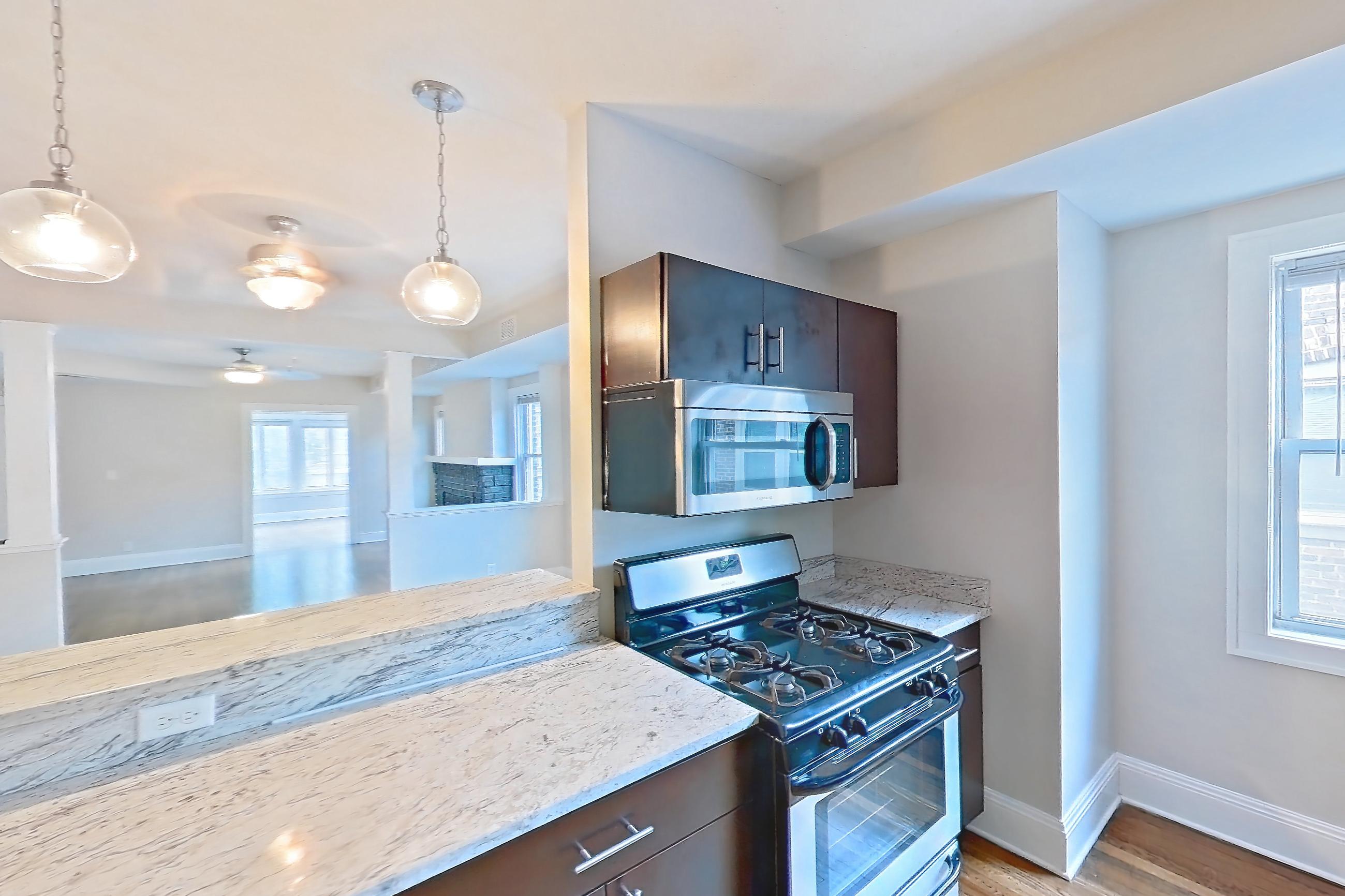 Kitchen with dark wood-finish flooring, dishwasher, gas range, light countertops, light stone countertops, light wood-finish flooring, microwave, oven/range, refrigerator, and stainless steel appliances, Apartment 5 at Integrity Cleveland Heights 
