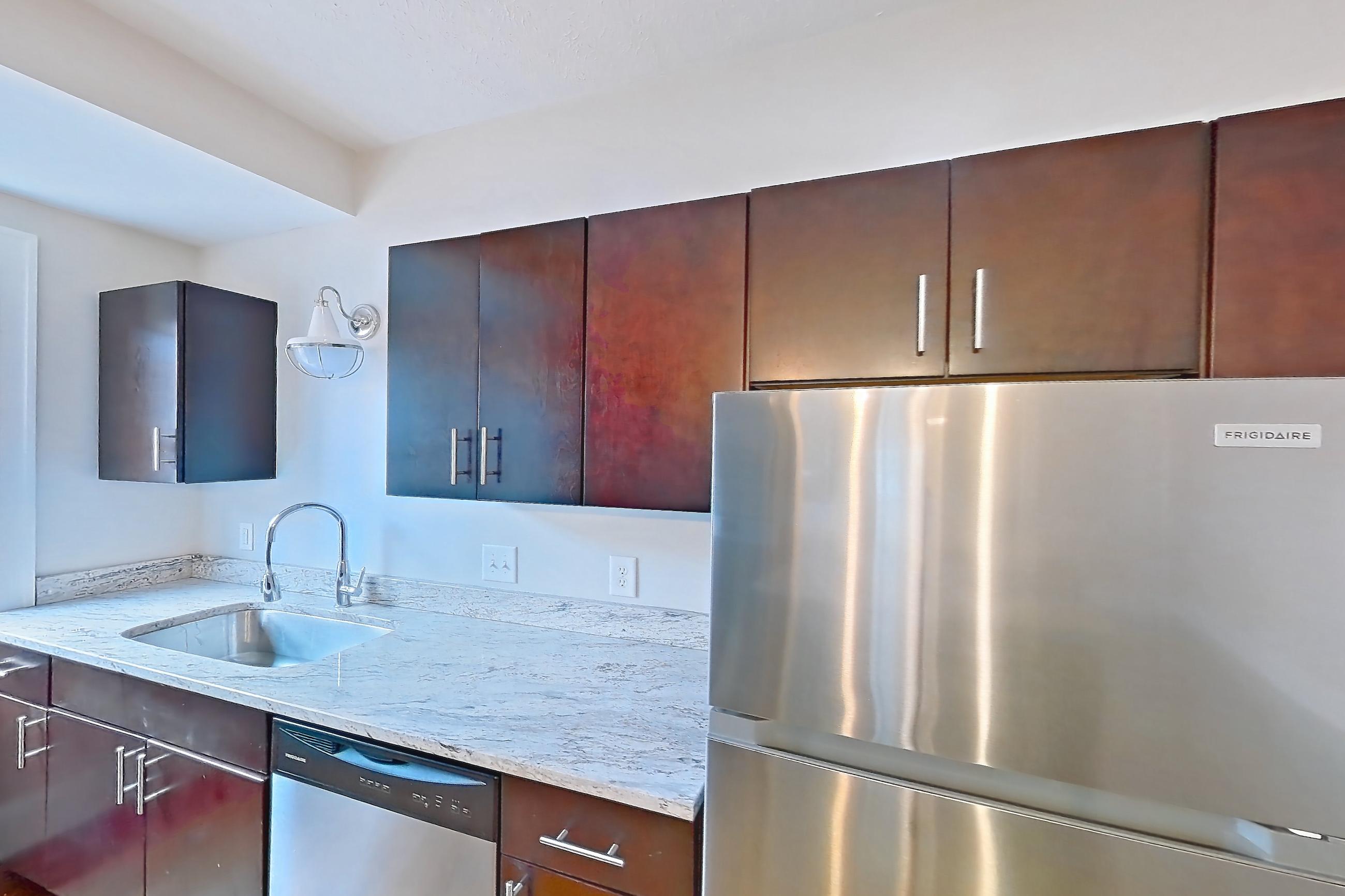 Kitchen with dark wood-finish flooring, dishwasher, gas range, light countertops, light stone countertops, light wood-finish flooring, microwave, oven/range, refrigerator, and stainless steel appliances, Apartment 5 at Integrity Cleveland Heights 