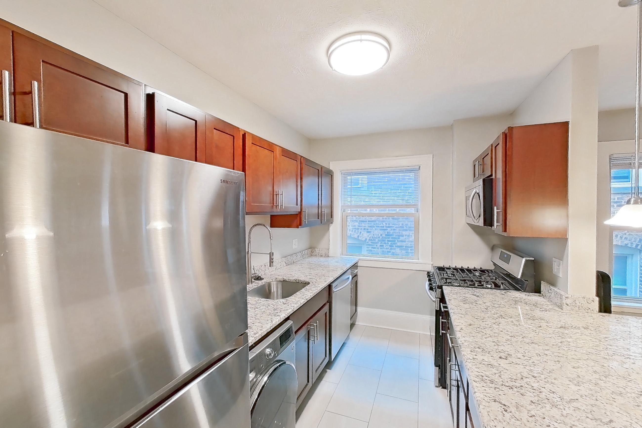 Kitchen with dishwasher, gas range, in-unit laundry, light countertops, light stone countertops, light wood-finish flooring, oven/range, refrigerator, and stainless steel appliances, Apartment 302 at Integrity Cleveland Heights
