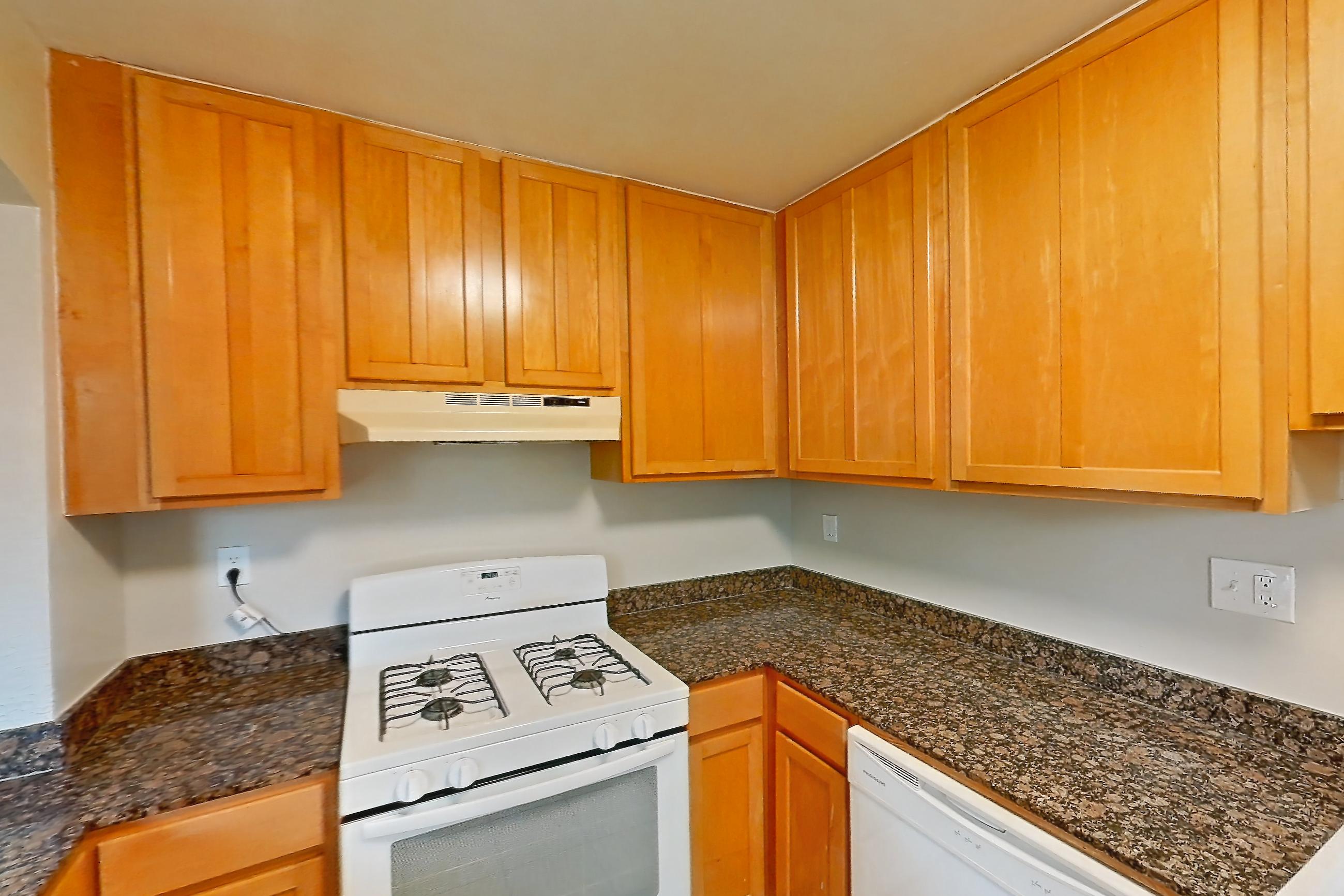 Kitchen with dark stone countertops, dishwasher, gas range, light tile flooring, light wood-finish flooring, oven/range, refrigerator, white appliances, and wood-finish flooring, Apartment 201 at Integrity Cleveland Heights