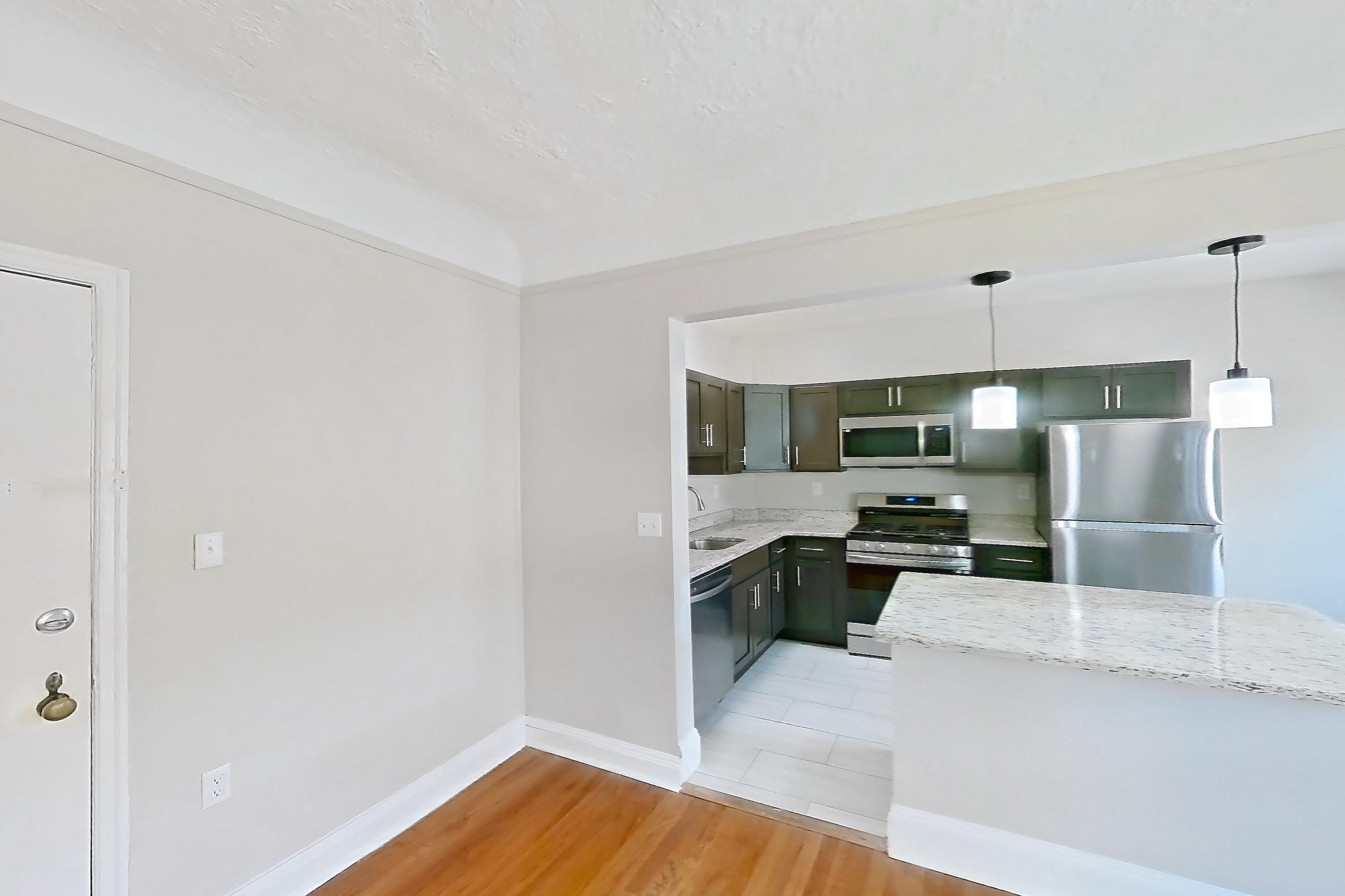 Living room with dishwasher, gas range, light stone countertops, light wood-finish flooring, oven/range, radiator heat, refrigerator, stainless steel appliances, and wood-finish flooring, Apartment 403 at Integrity Gold Coast