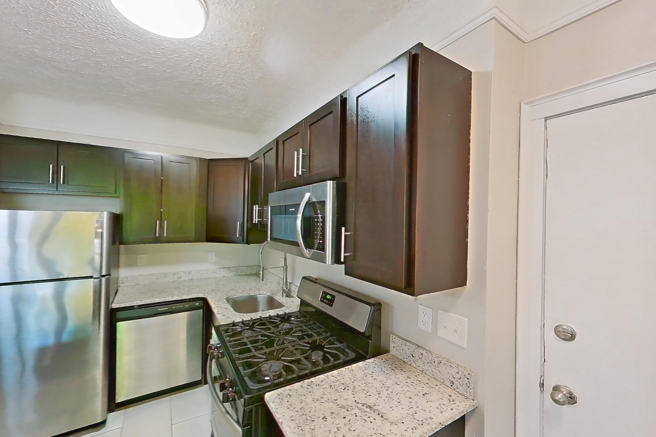 Kitchen with dishwasher, gas range, light countertops, light stone countertops, light tile flooring, light wood-finish flooring, microwave, oven/range, radiator heat, refrigerator, and stainless steel appliances, Apartment 302 at Integrity Gold Coast