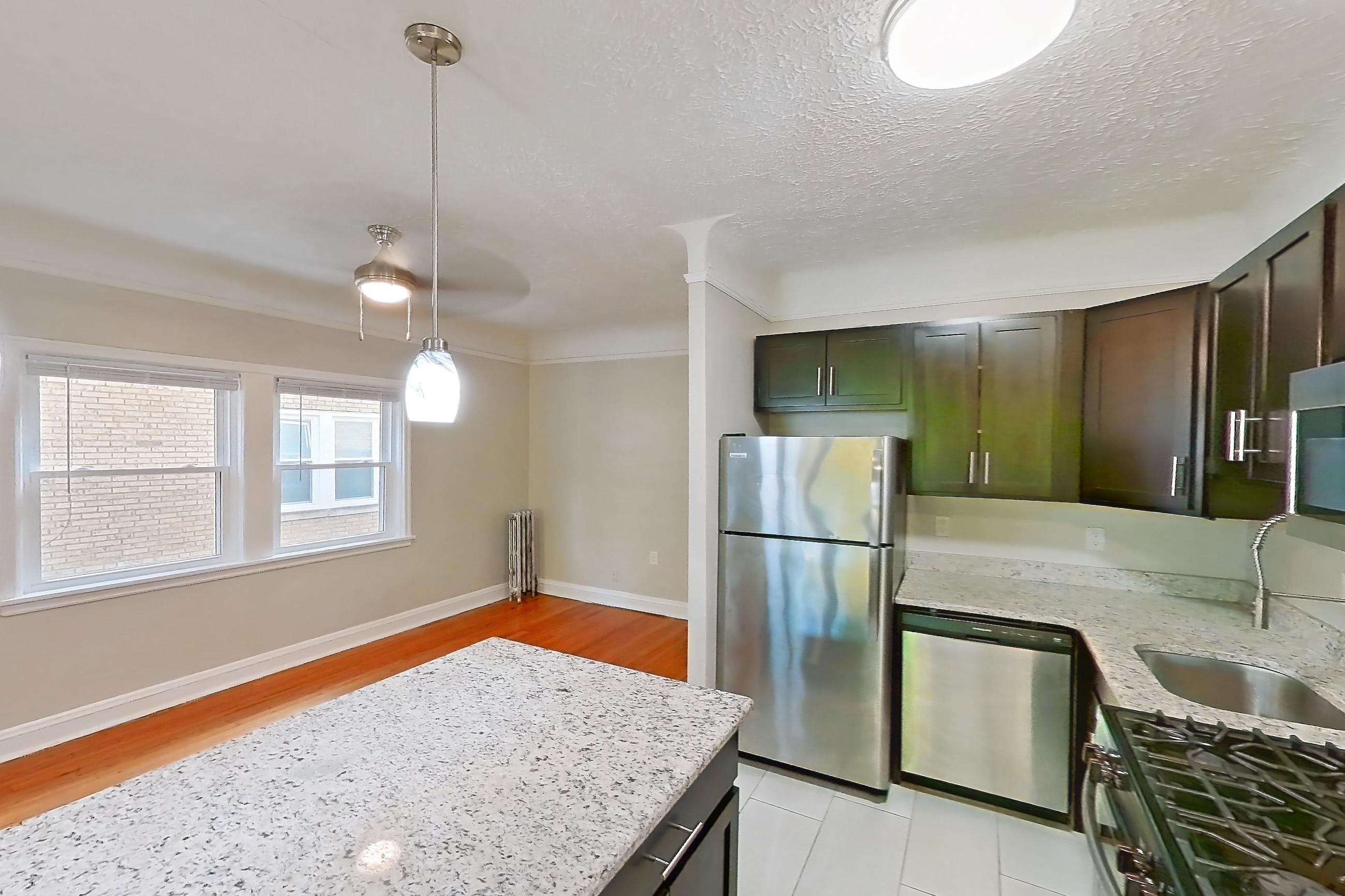 Kitchen with dishwasher, gas range, light countertops, light stone countertops, light tile flooring, light wood-finish flooring, microwave, oven/range, radiator heat, refrigerator, and stainless steel appliances, Apartment 302 at Integrity Gold Coast