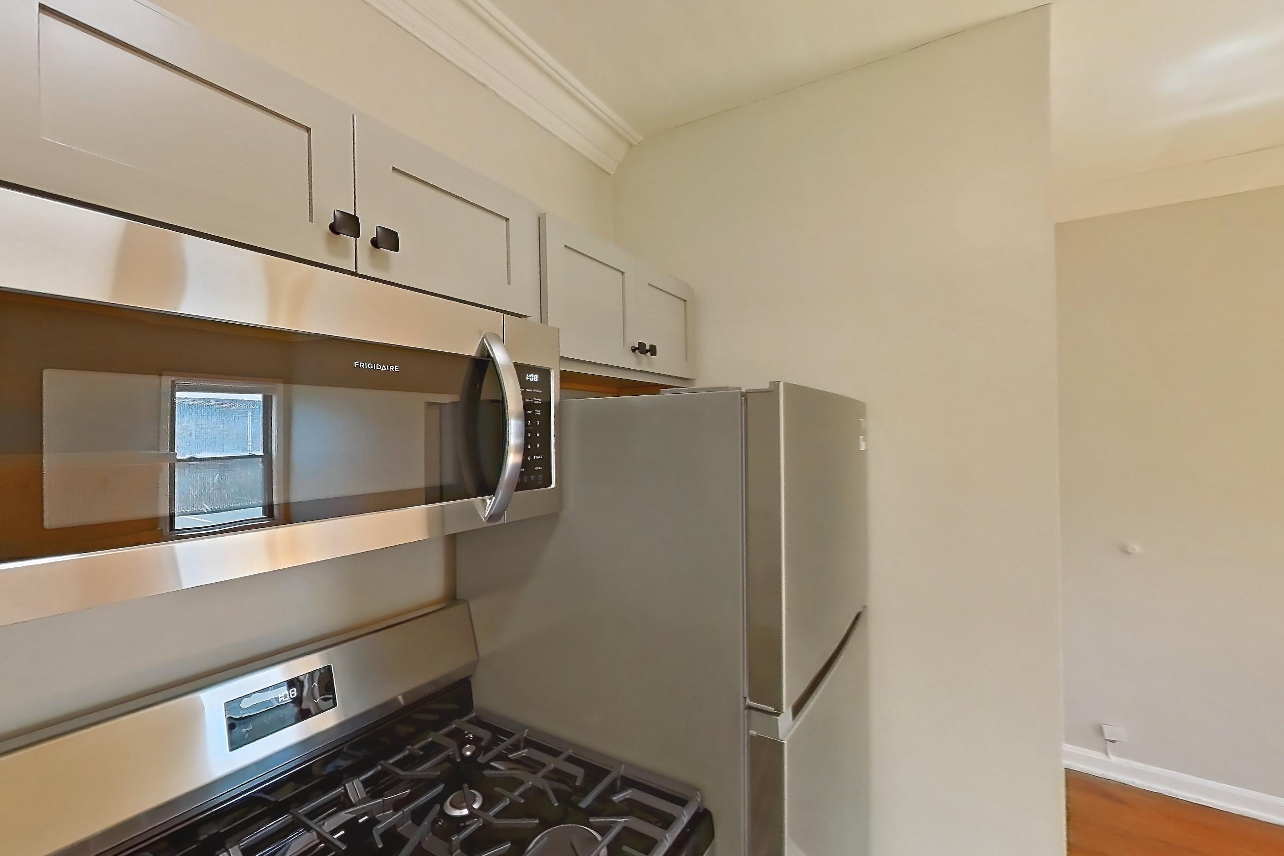 Kitchen with gas range, light countertops, light stone countertops, light tile flooring, light wood-finish flooring, oven/range, radiator heat, and stainless steel appliances, Apartment 11-17 at Integrity Gold Coast