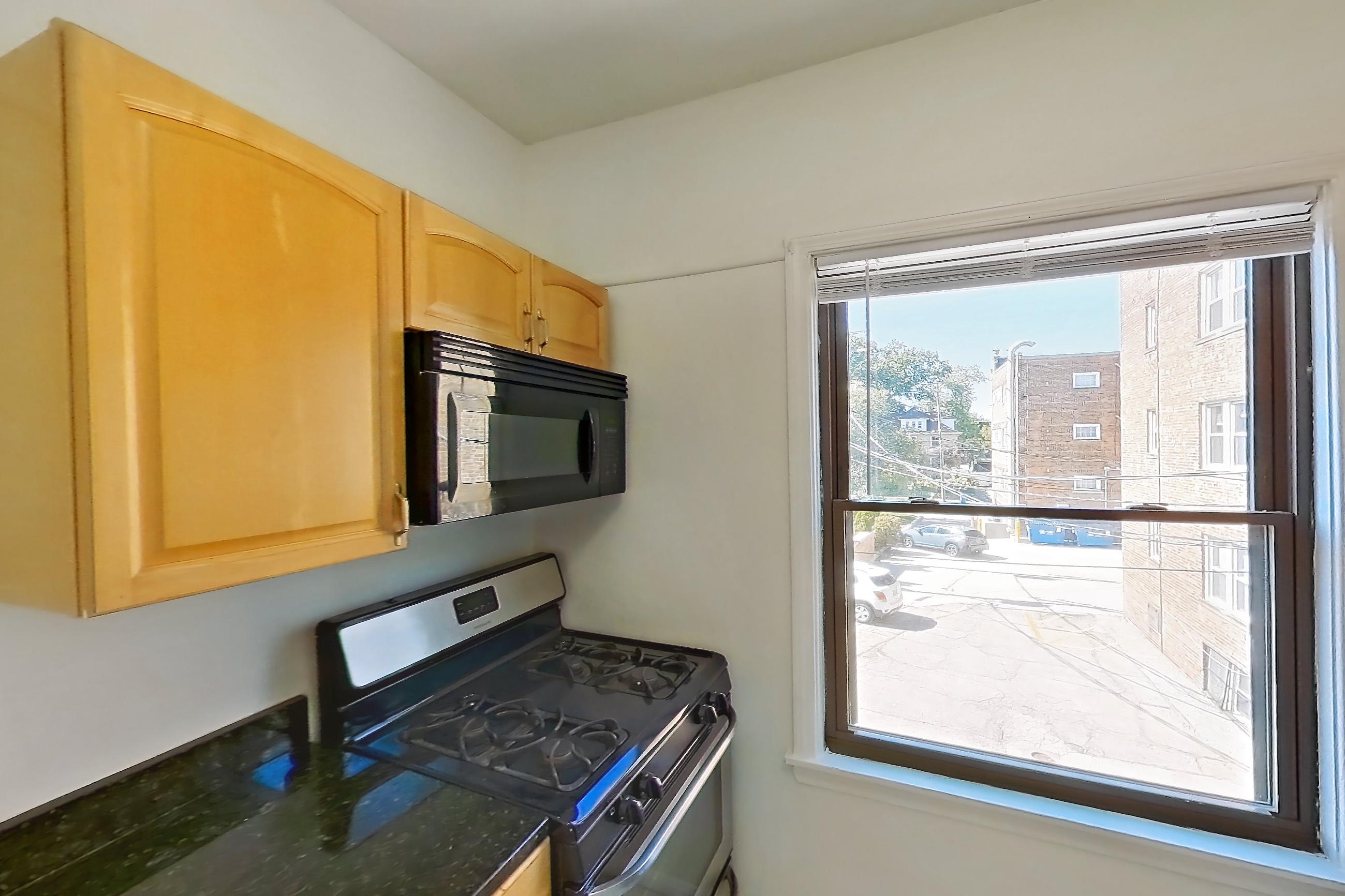 Kitchen with black appliances, dark stone countertops, gas range, light countertops, light tile flooring, microwave, oven/range, refrigerator, and stainless steel appliances, Apartment 13-10 at Integrity Gold Coast