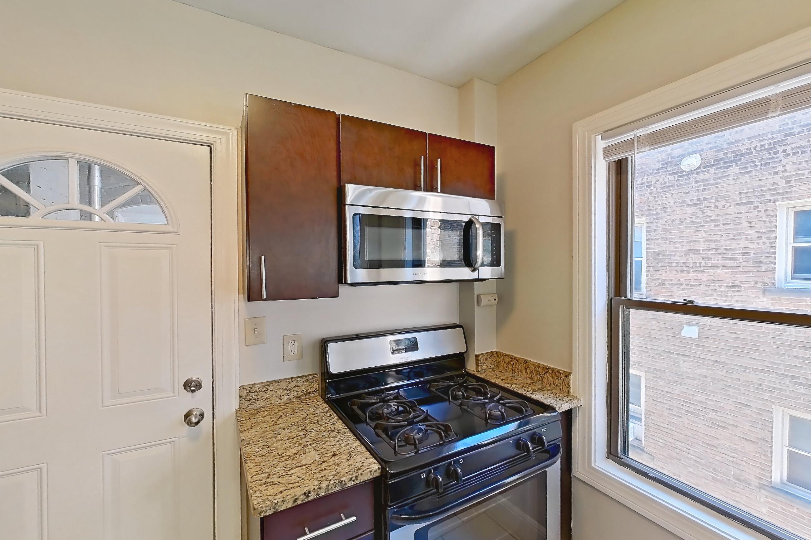Kitchen with black appliances, dishwasher, gas range, light countertops, light stone countertops, light tile flooring, microwave, oven/range, refrigerator, and stainless steel appliances, Apartment 15-3 at Integrity Gold Coast