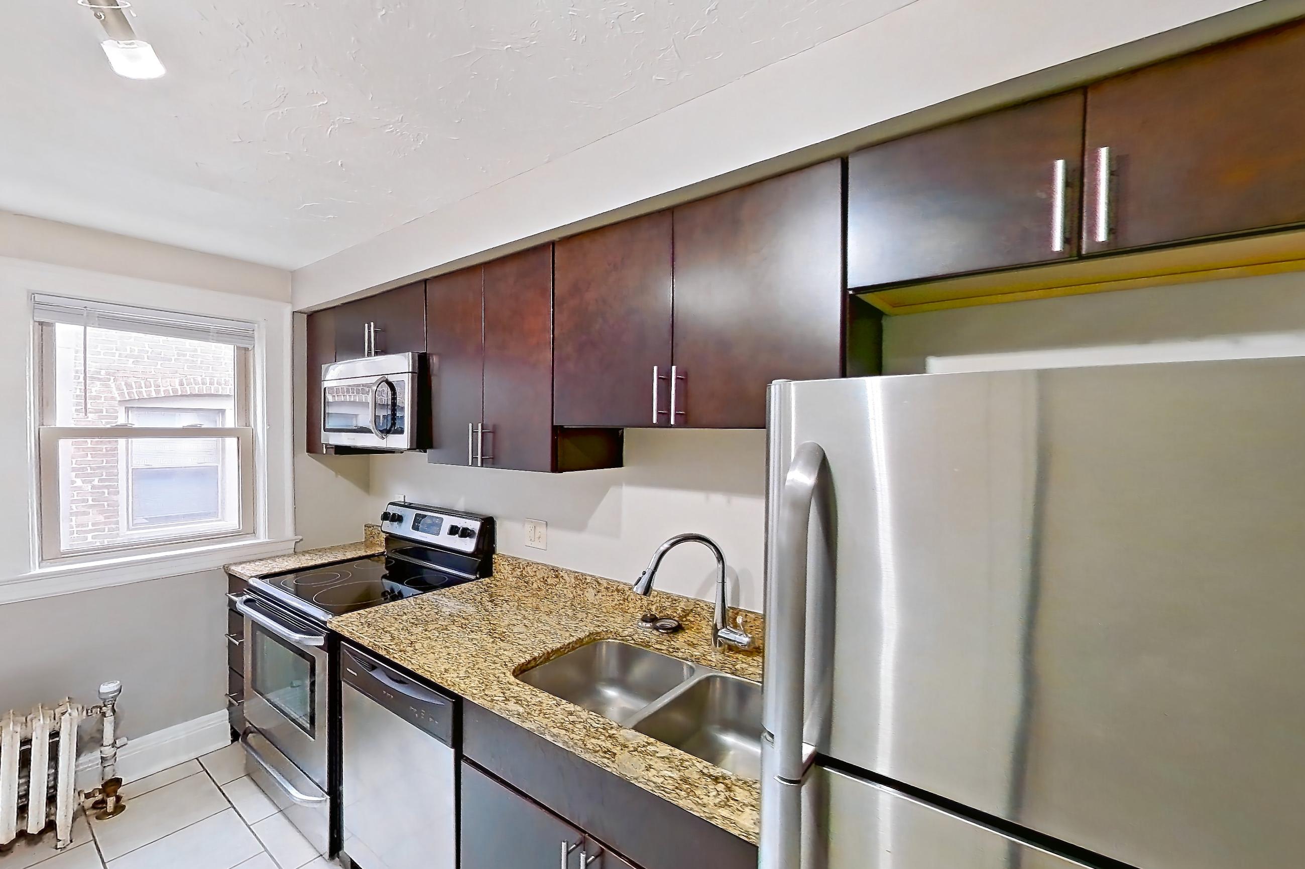 Kitchen with electric range, light countertops, light stone countertops, light tile flooring, oven/range, radiator heat, refrigerator, and stainless steel appliances, Apartment 8 at Integrity Gold Coast