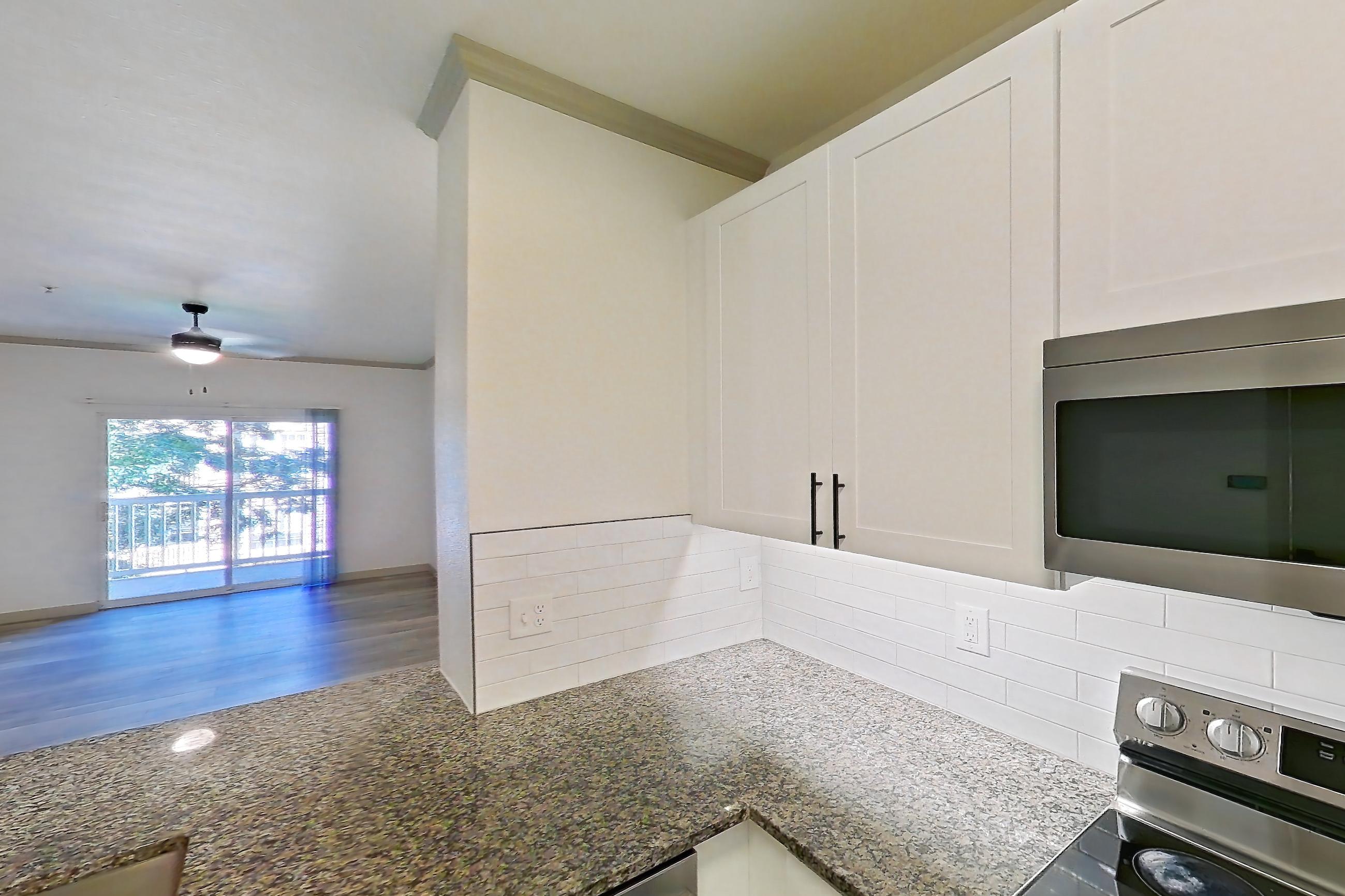 Kitchen with dark stone countertops, dishwasher, electric range, light countertops, light stone countertops, light wood-finish flooring, microwave, oven/range, refrigerator, and stainless steel appliances, Apartment 10-208 at Cortland Westminster
