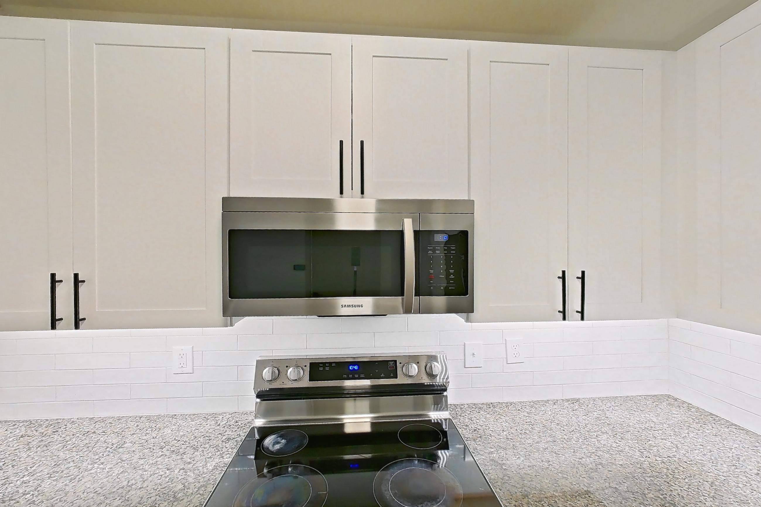 Kitchen with dark stone countertops, dishwasher, electric range, light countertops, light stone countertops, light wood-finish flooring, microwave, oven/range, refrigerator, and stainless steel appliances, Apartment 10-208 at Cortland Westminster