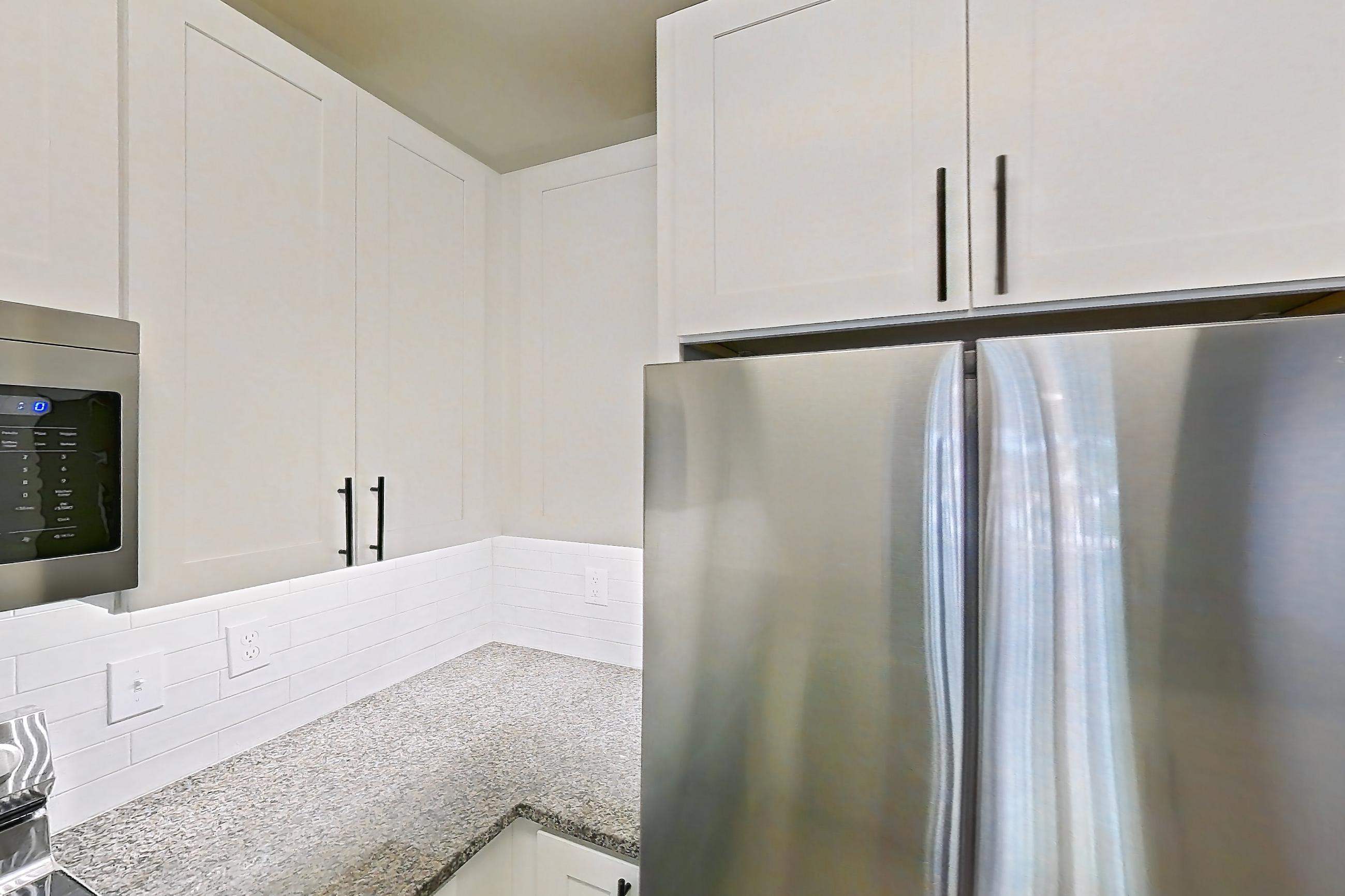 Kitchen with dark stone countertops, dishwasher, electric range, light countertops, light stone countertops, light wood-finish flooring, microwave, oven/range, refrigerator, and stainless steel appliances, Apartment 10-208 at Cortland Westminster
