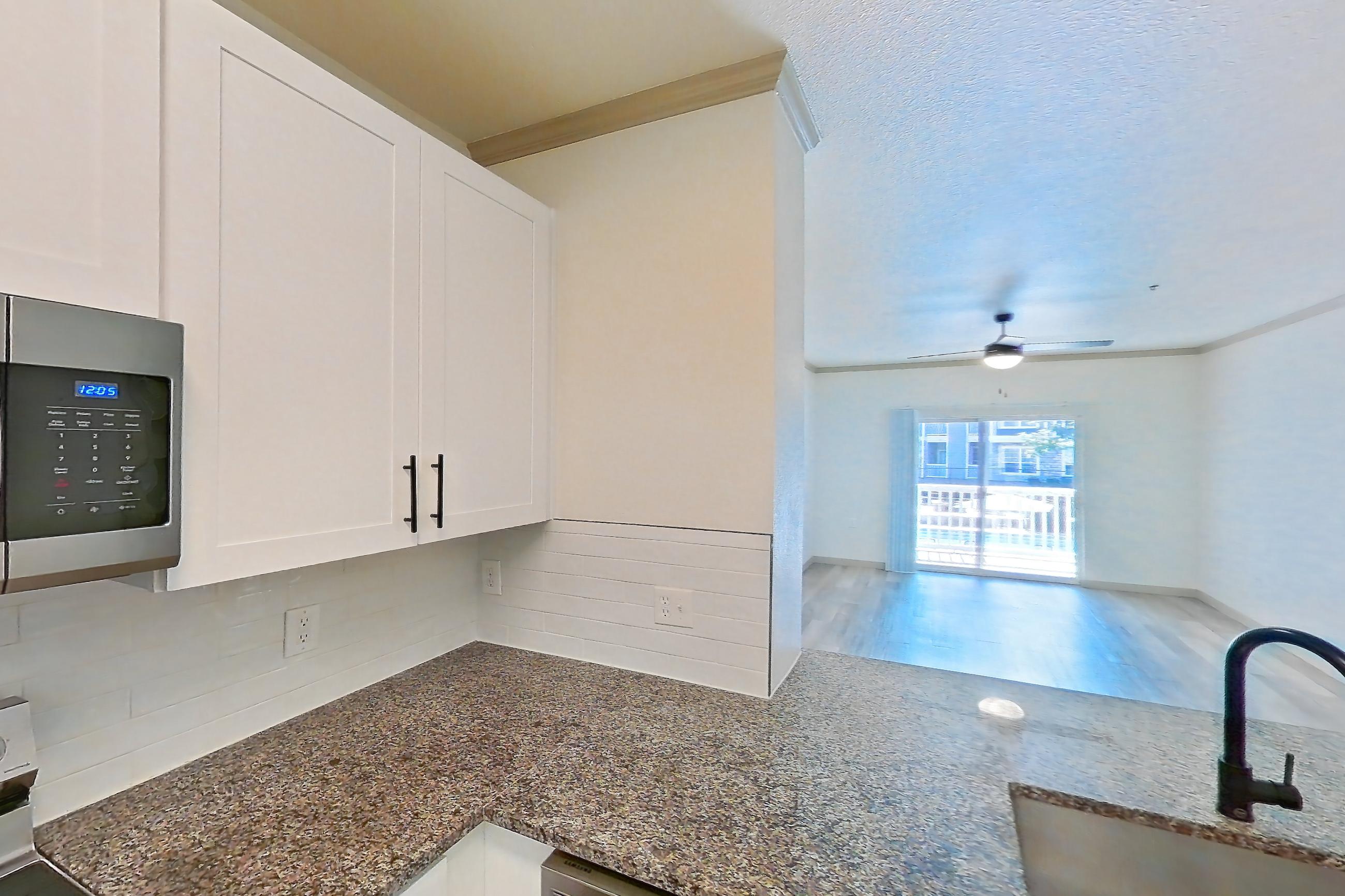 Kitchen with dark stone countertops, dishwasher, electric range, light countertops, light wood-finish flooring, microwave, oven/range, refrigerator, and stainless steel appliances, Apartment 17-205 at Cortland Westminster