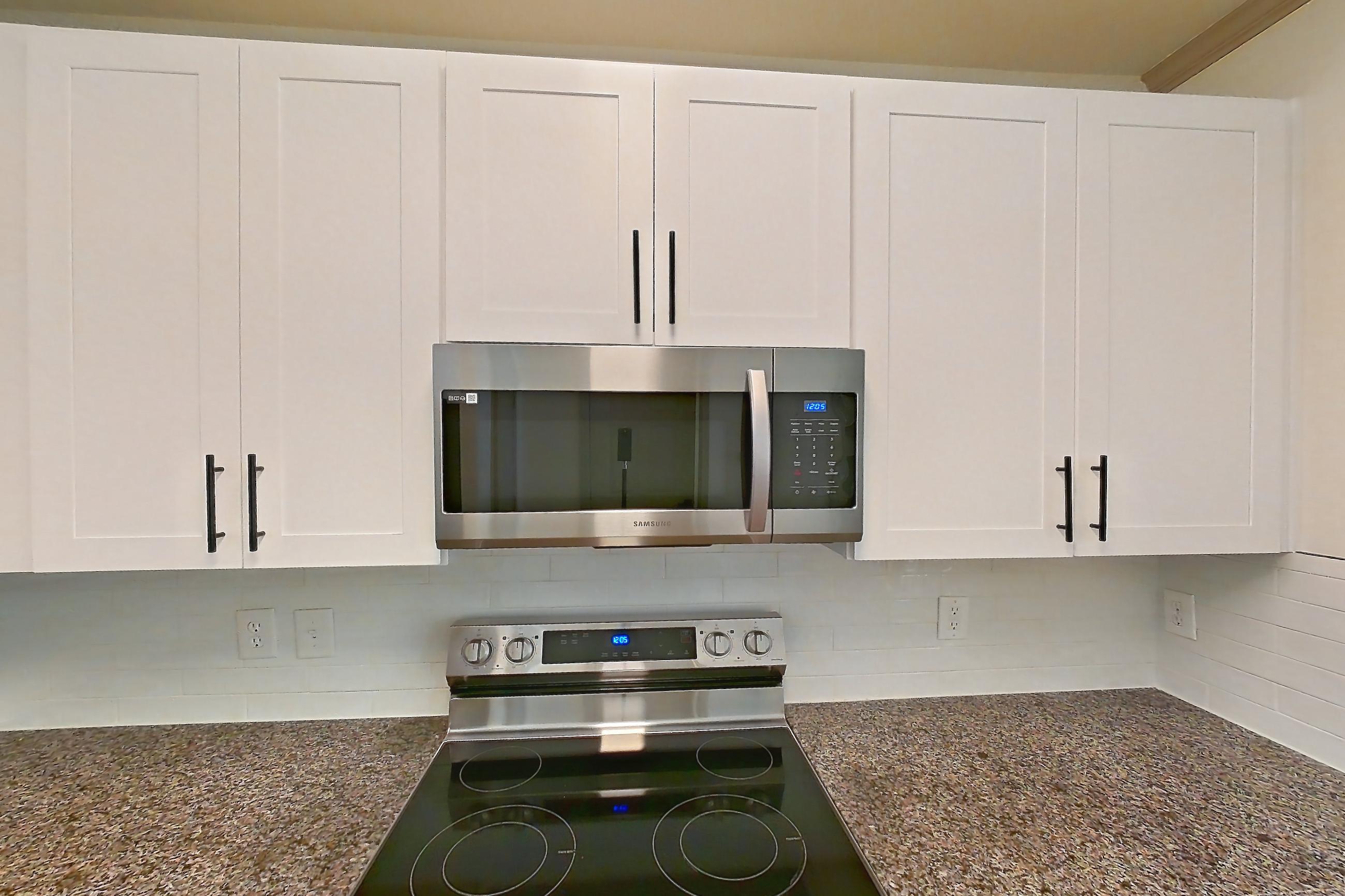 Kitchen with dark stone countertops, dishwasher, electric range, light countertops, light wood-finish flooring, microwave, oven/range, refrigerator, and stainless steel appliances, Apartment 17-205 at Cortland Westminster