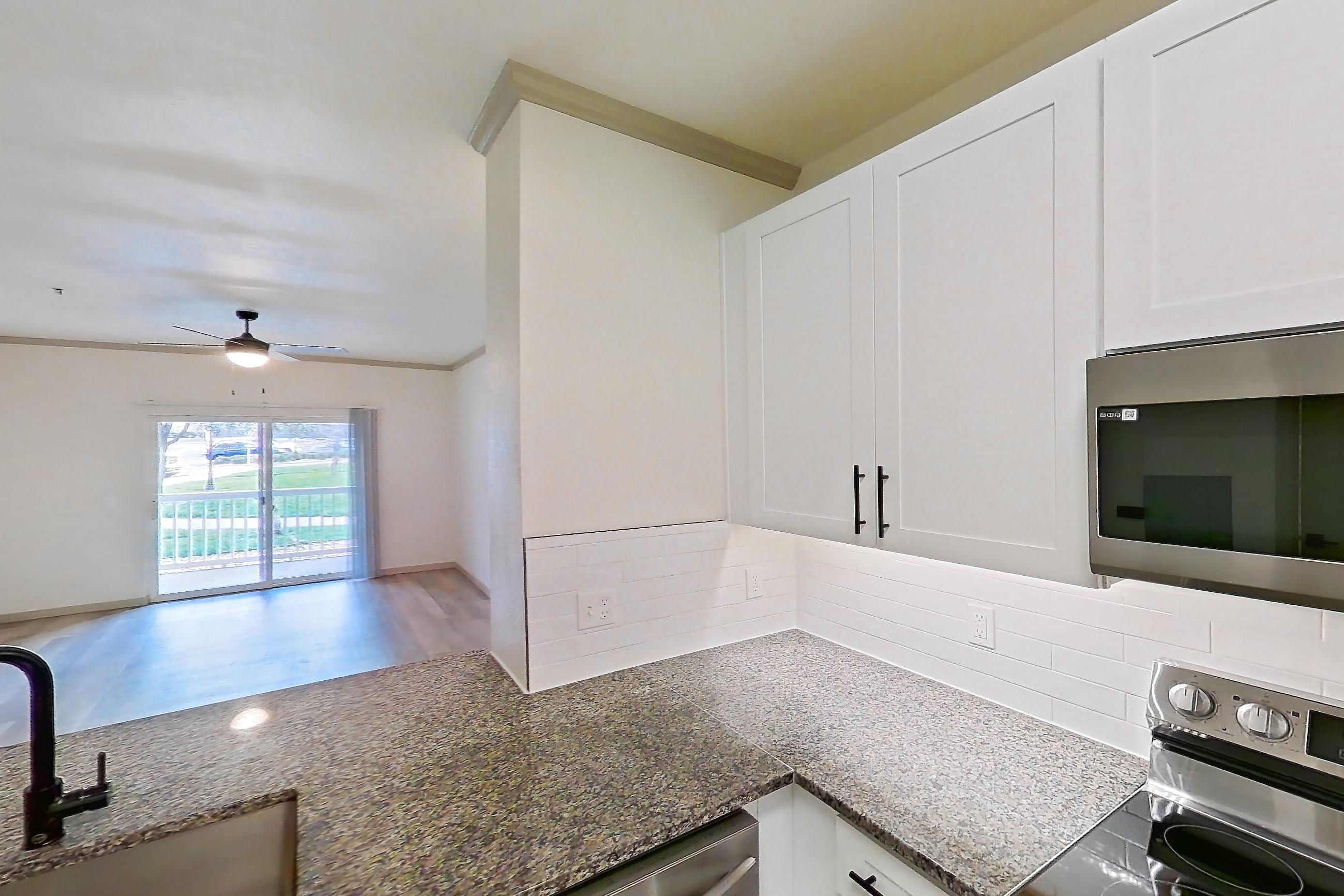 Kitchen with dark stone countertops, dishwasher, electric range, light countertops, light stone countertops, light wood-finish flooring, microwave, oven/range, refrigerator, and stainless steel appliances, Apartment 18-108 at Cortland Westminster