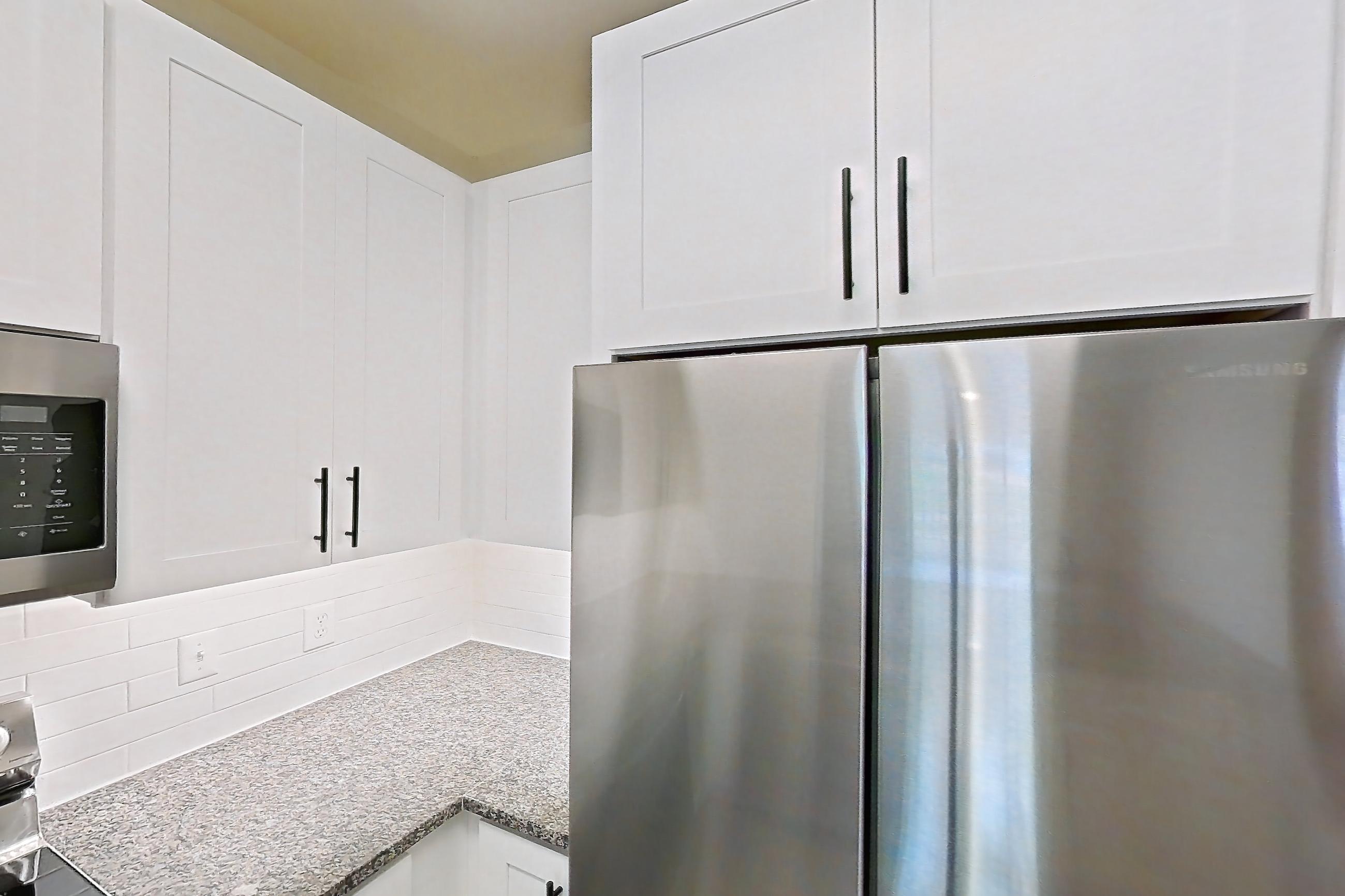 Kitchen with dark stone countertops, dishwasher, electric range, light countertops, light stone countertops, light wood-finish flooring, microwave, oven/range, refrigerator, and stainless steel appliances, Apartment 18-108 at Cortland Westminster