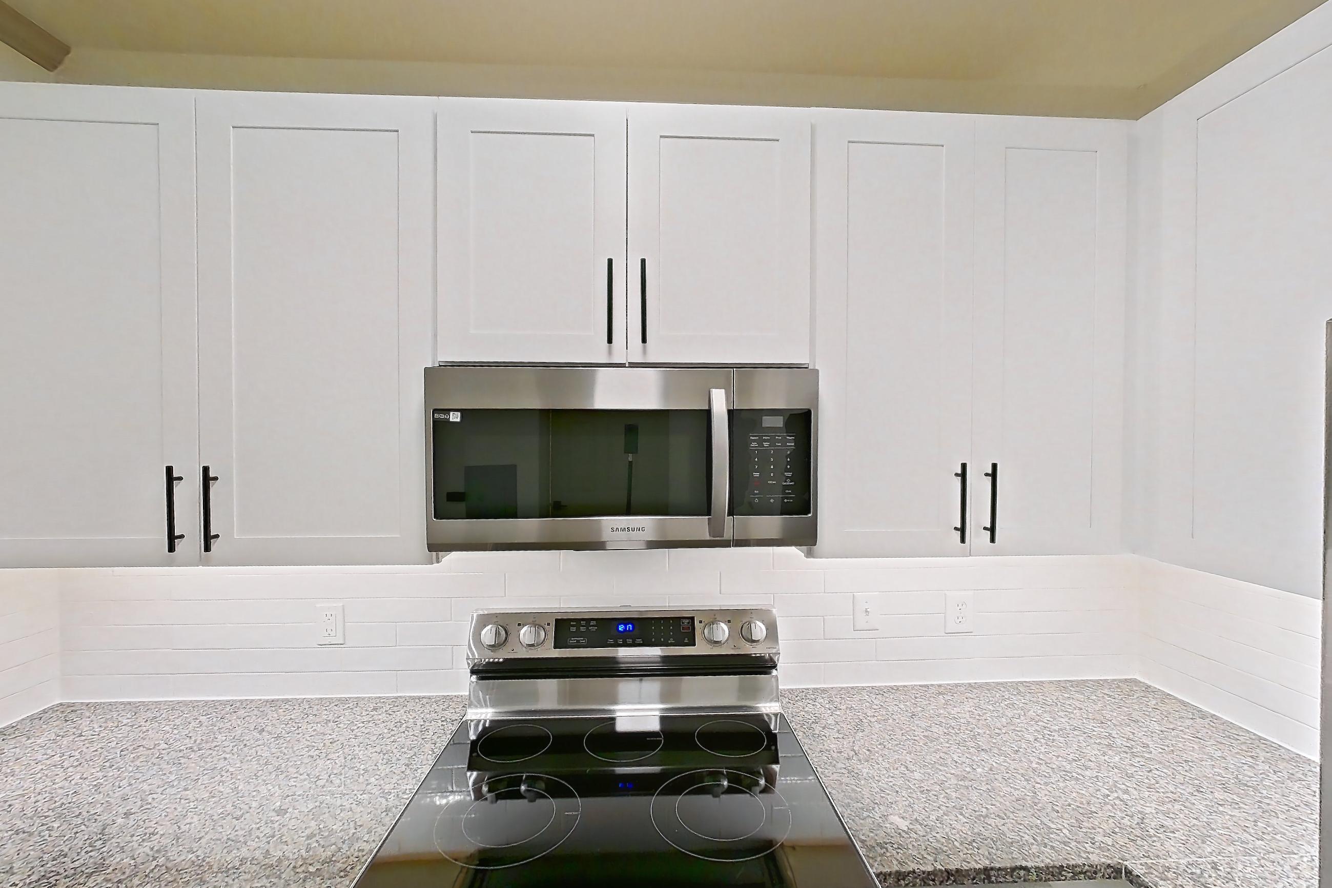 Kitchen with dark stone countertops, dishwasher, electric range, light countertops, light stone countertops, light wood-finish flooring, microwave, oven/range, refrigerator, and stainless steel appliances, Apartment 18-108 at Cortland Westminster