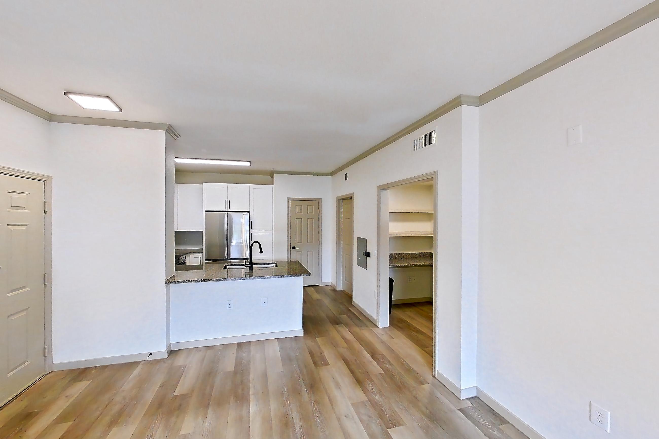 Living space with dark stone countertops, light wood-finish flooring, refrigerator, and stainless steel appliances, Apartment 18-108 at Cortland Westminster