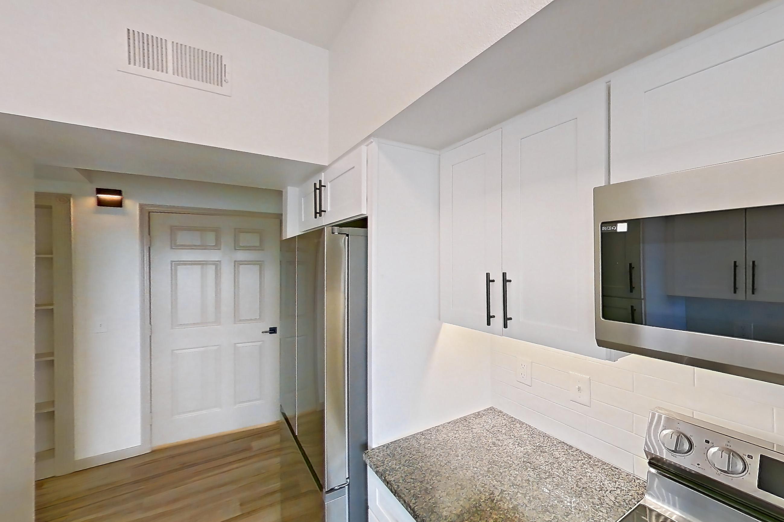 Kitchen with dark stone countertops, dishwasher, electric range, light countertops, light wood-finish flooring, microwave, oven/range, refrigerator, and stainless steel appliances, Apartment 08-302 at Cortland Westminster