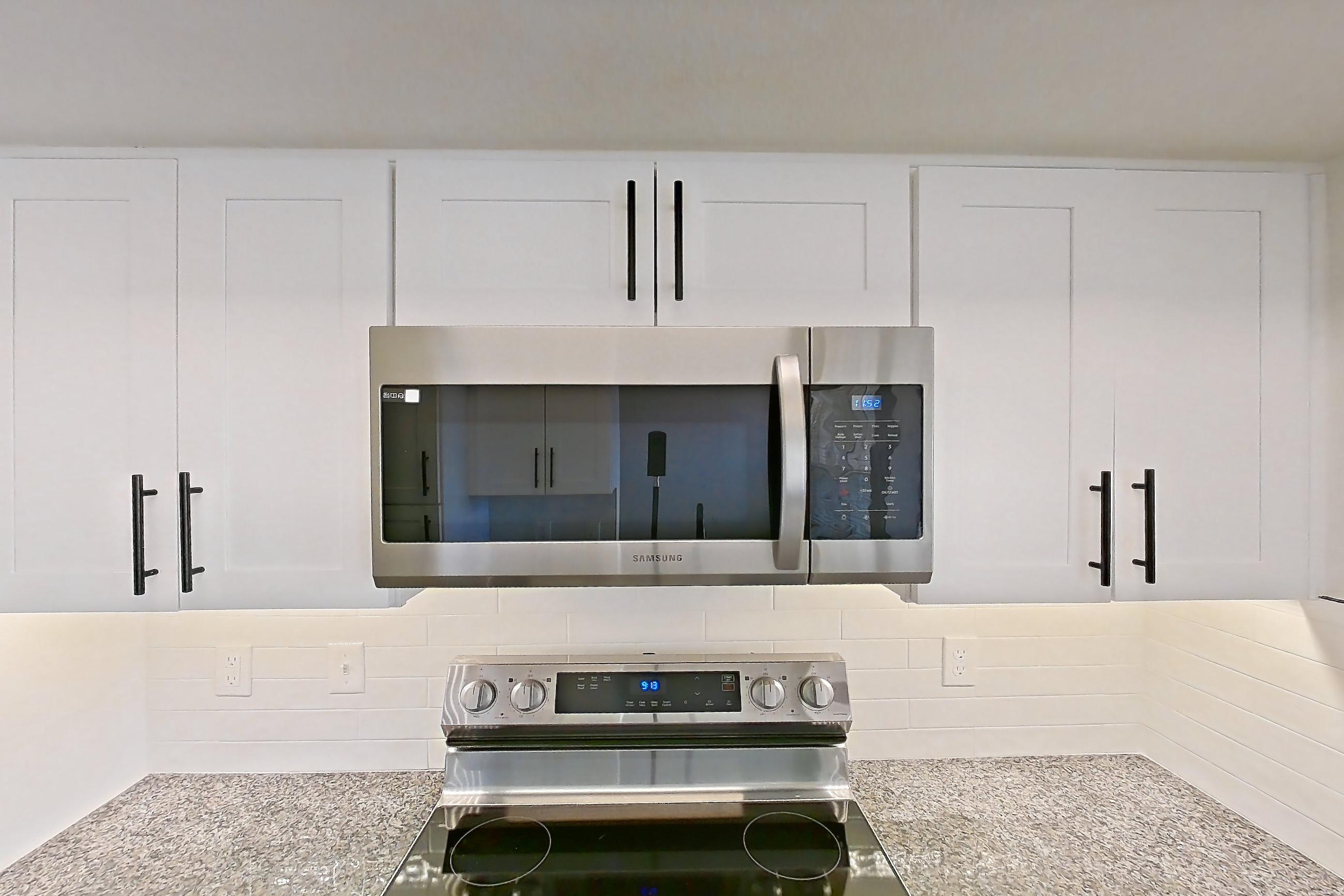 Kitchen with dark stone countertops, dishwasher, electric range, light countertops, light wood-finish flooring, microwave, oven/range, refrigerator, and stainless steel appliances, Apartment 08-302 at Cortland Westminster