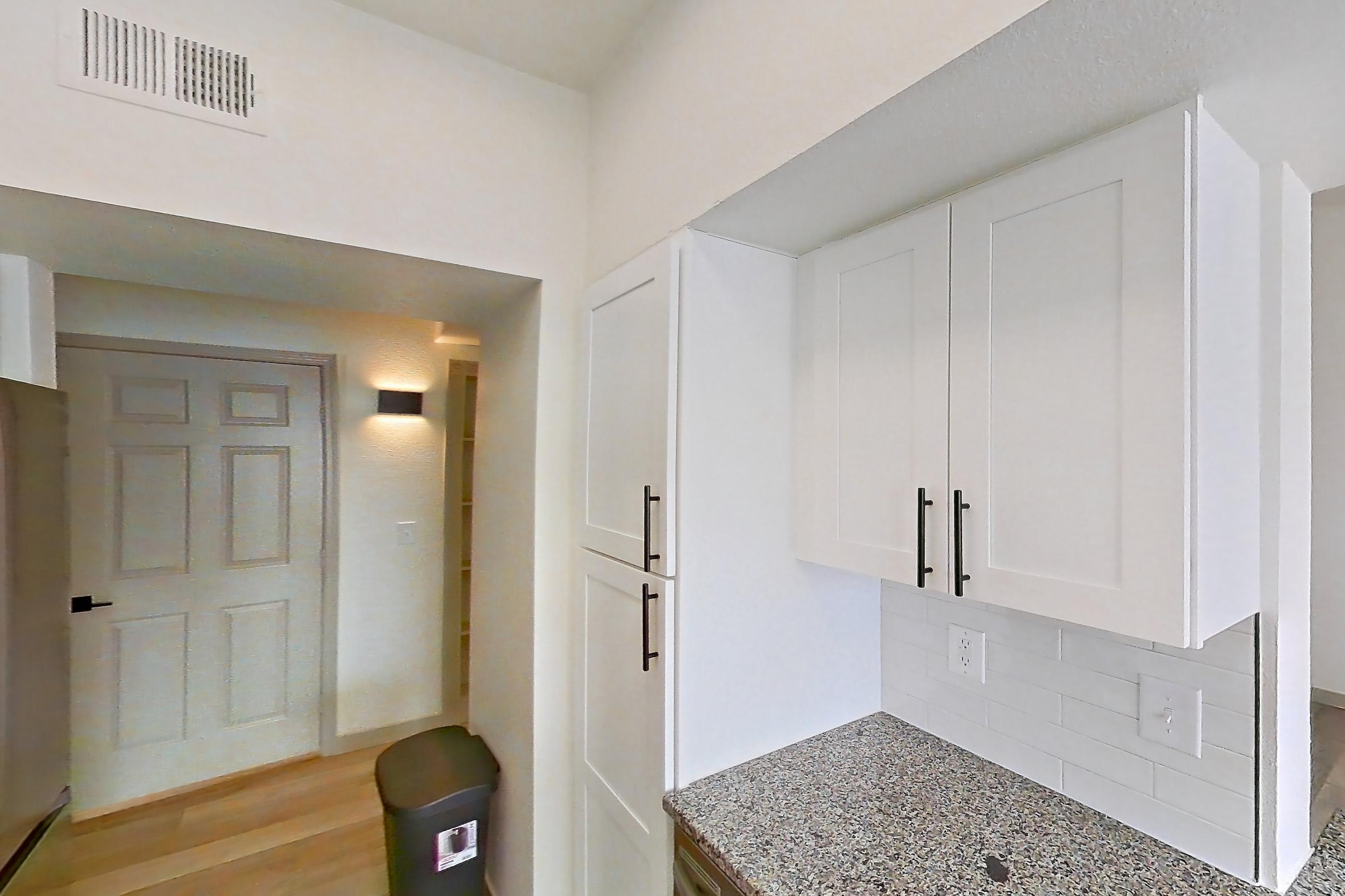 Kitchen with dark stone countertops, dishwasher, electric range, light countertops, light stone countertops, light wood-finish flooring, microwave, oven/range, refrigerator, and stainless steel appliances, Apartment 16-303 at Cortland Westminster