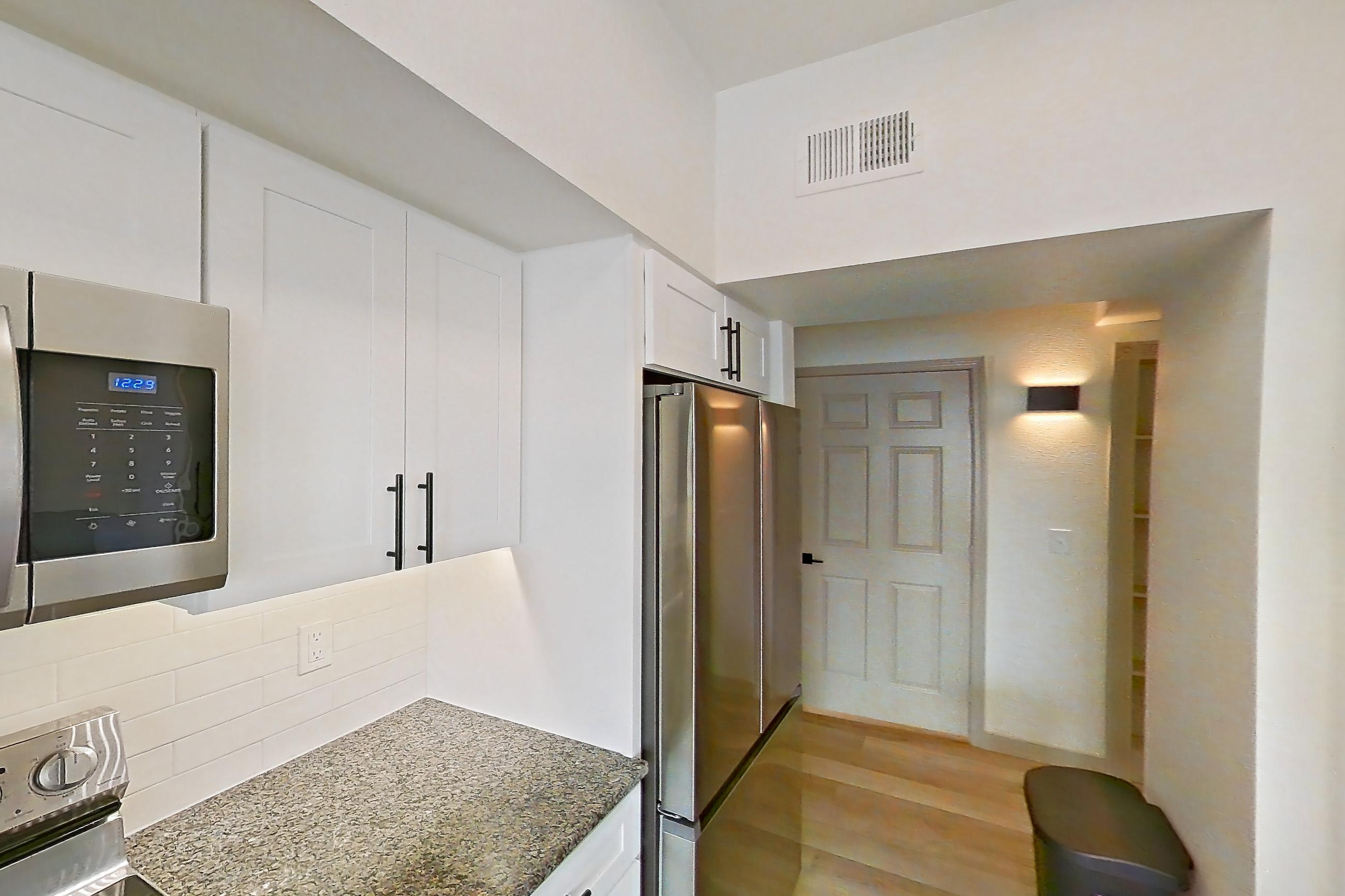 Kitchen with dark stone countertops, dishwasher, electric range, light countertops, light stone countertops, light wood-finish flooring, microwave, oven/range, refrigerator, and stainless steel appliances, Apartment 16-303 at Cortland Westminster