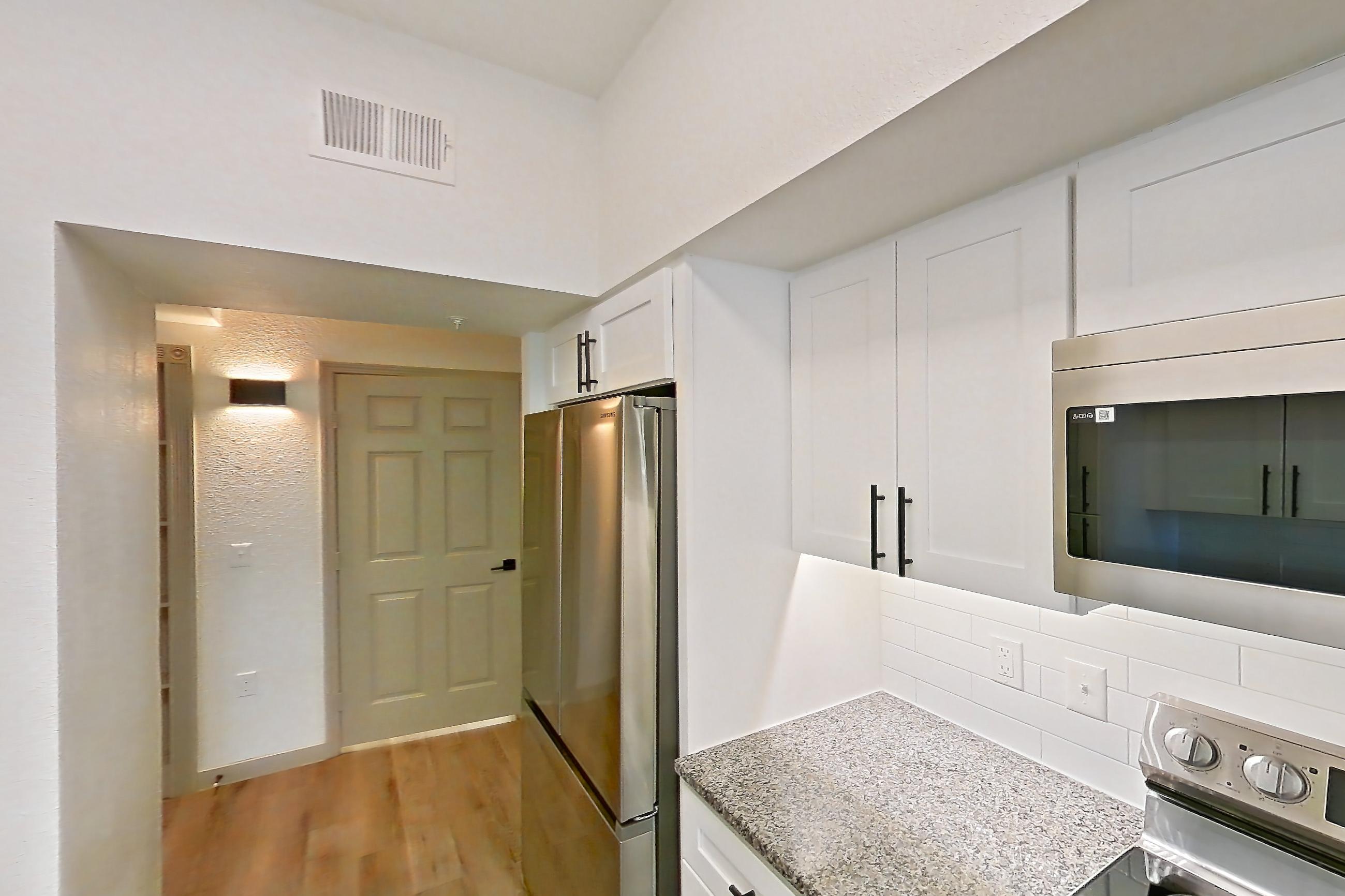 Kitchen with dishwasher, electric range, light countertops, light stone countertops, light wood-finish flooring, microwave, oven/range, refrigerator, and stainless steel appliances, Apartment 20-106 at Cortland Westminster