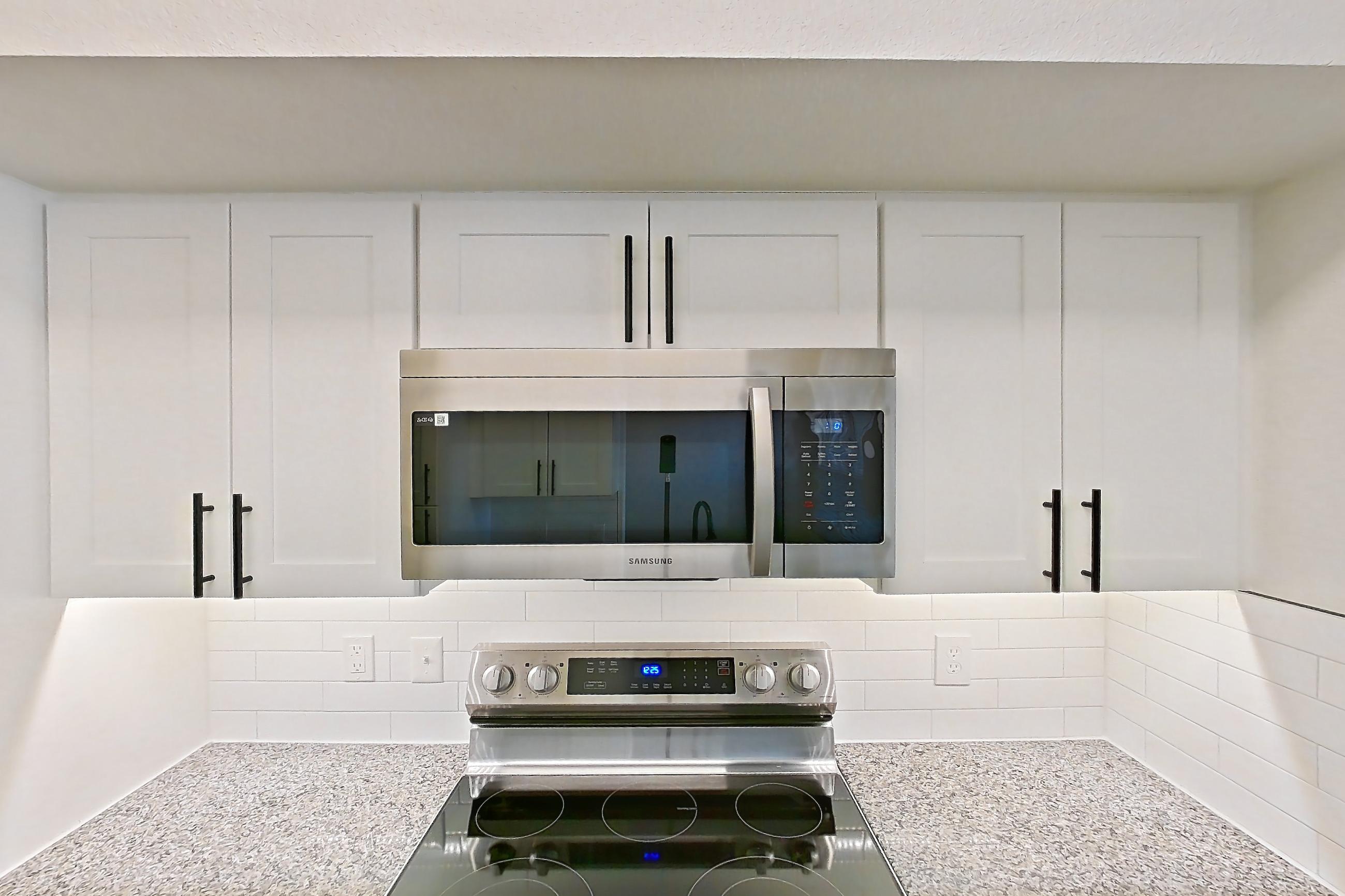 Kitchen with dishwasher, electric range, light countertops, light stone countertops, light wood-finish flooring, microwave, oven/range, refrigerator, and stainless steel appliances, Apartment 20-106 at Cortland Westminster