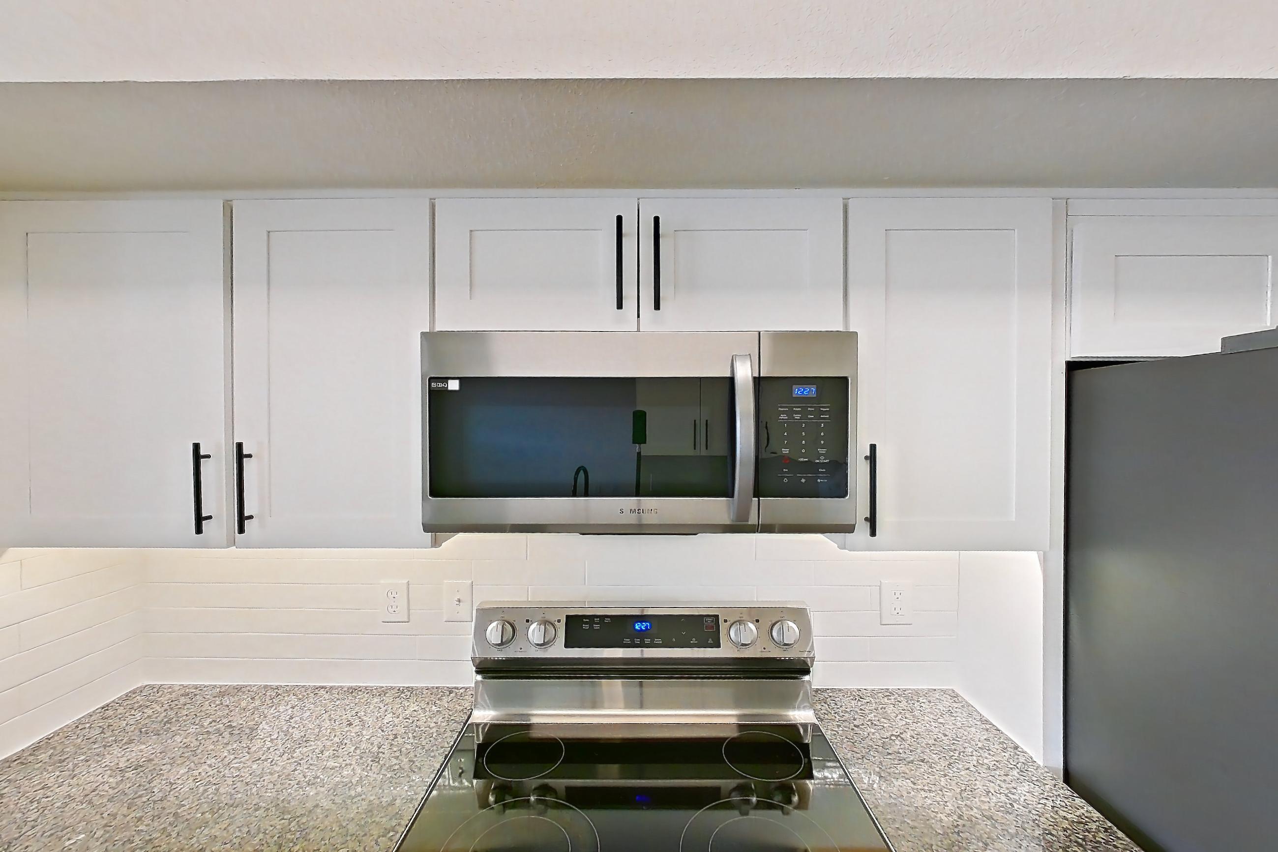 Kitchen with dark stone countertops, dishwasher, electric range, light wood-finish flooring, microwave, oven/range, refrigerator, and stainless steel appliances, Apartment 19-208 at Cortland Westminster