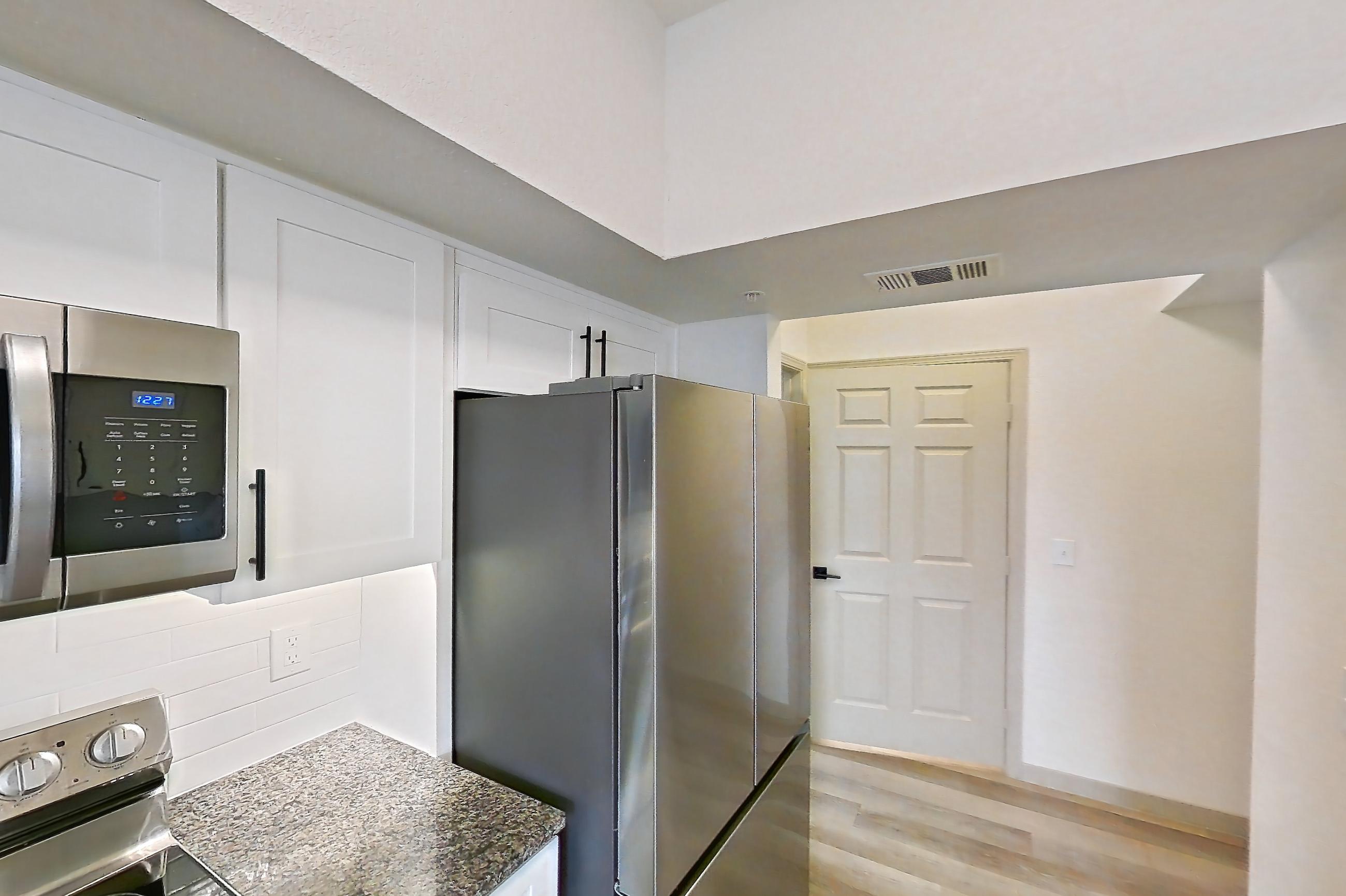 Kitchen with dark stone countertops, dishwasher, electric range, light wood-finish flooring, microwave, oven/range, refrigerator, and stainless steel appliances, Apartment 19-208 at Cortland Westminster