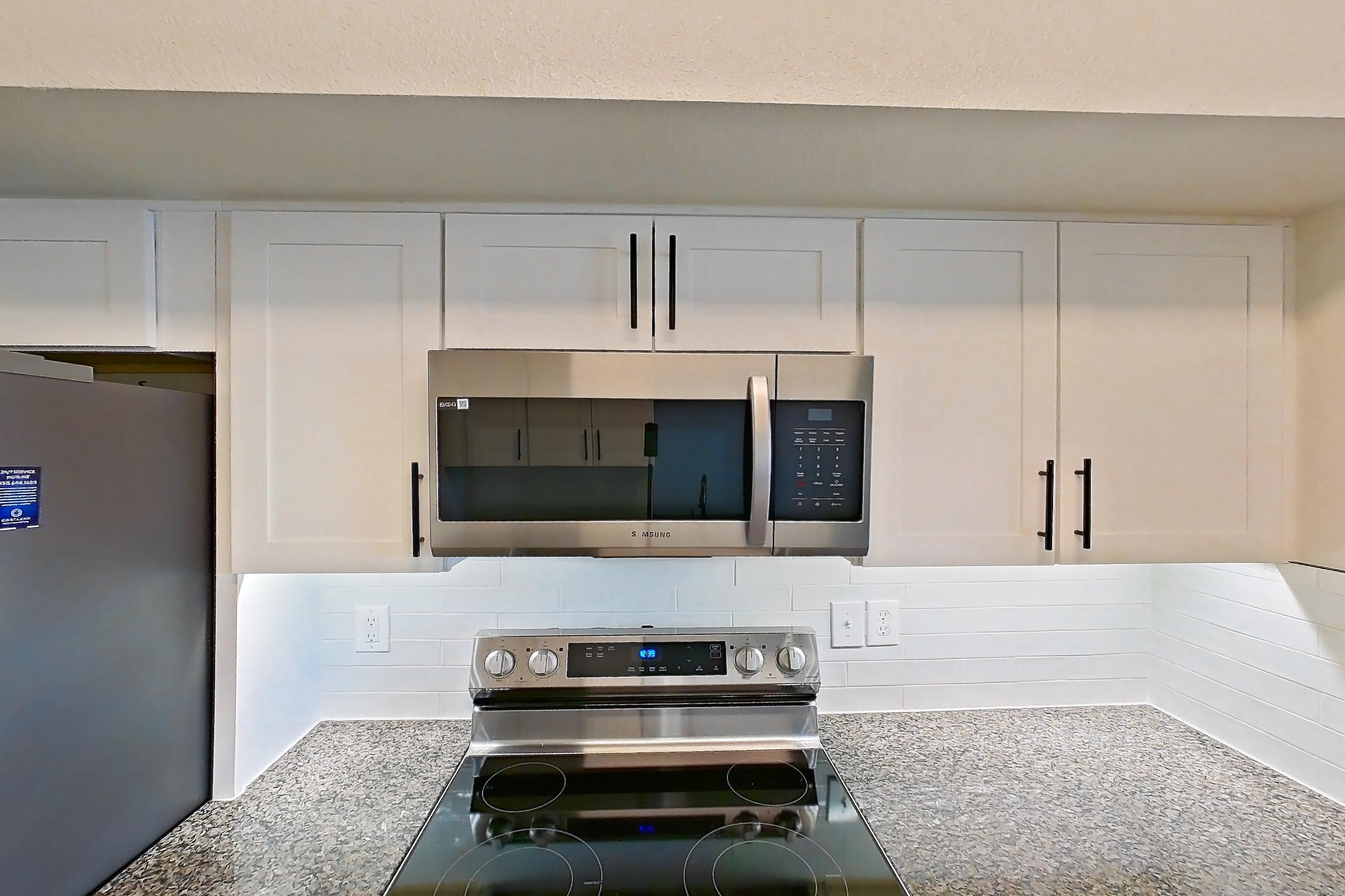 Kitchen with dark stone countertops, dishwasher, electric range, light wood-finish flooring, microwave, oven/range, refrigerator, and stainless steel appliances, Apartment 21-205 at Cortland Westminster