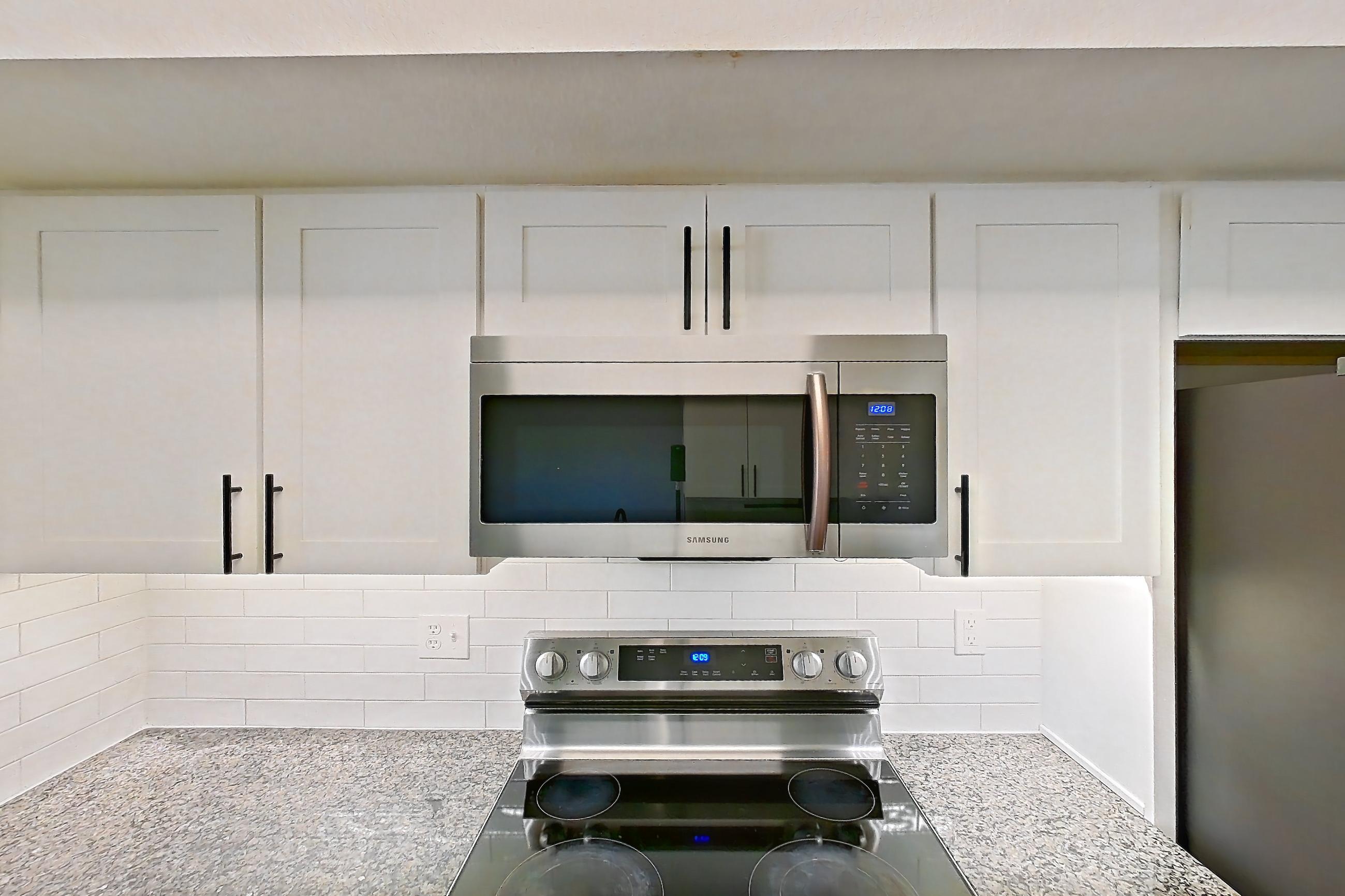 Kitchen with dark stone countertops, dishwasher, electric range, light countertops, light wood-finish flooring, microwave, oven/range, refrigerator, and stainless steel appliances, Apartment 22-204 at Cortland Westminster