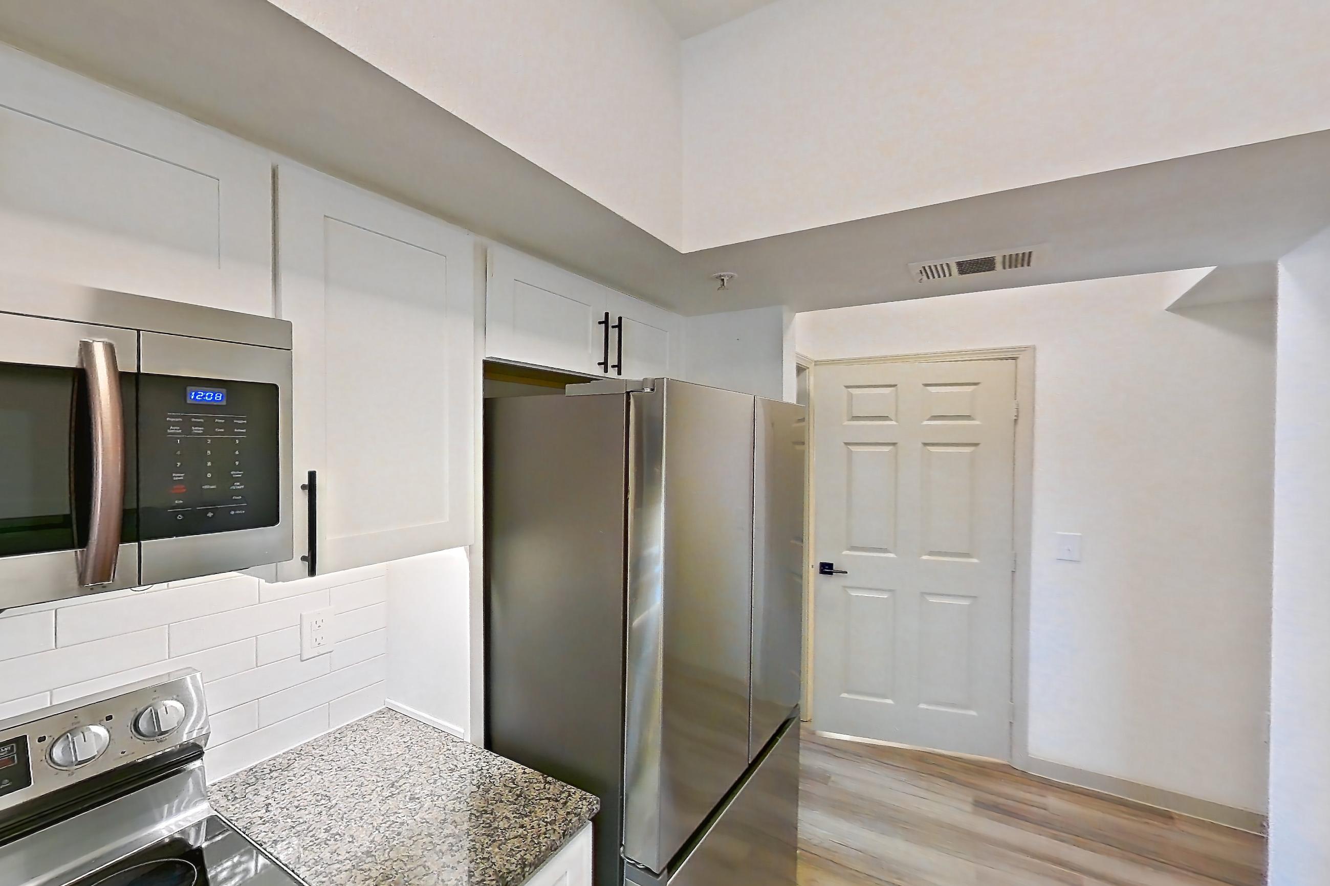 Kitchen with dark stone countertops, dishwasher, electric range, light countertops, light wood-finish flooring, microwave, oven/range, refrigerator, and stainless steel appliances, Apartment 22-204 at Cortland Westminster