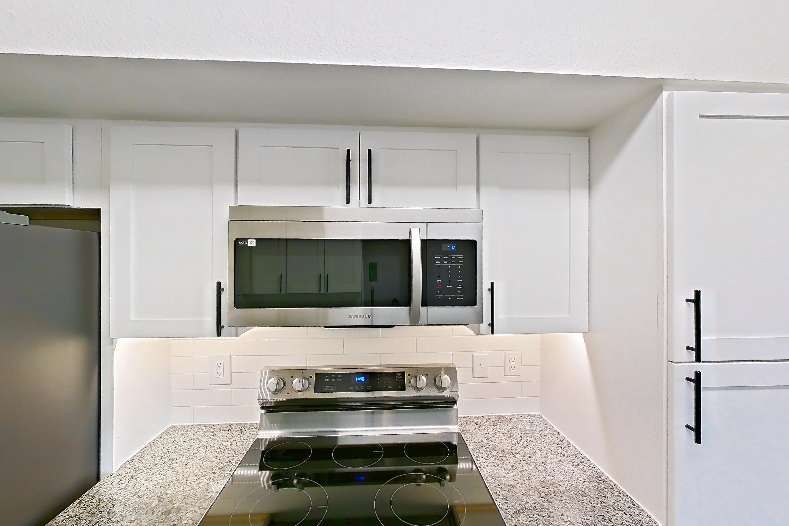 Kitchen with dishwasher, electric range, light stone countertops, light wood-finish flooring, microwave, oven/range, refrigerator, and stainless steel appliances, Apartment 23-201 at Cortland Westminster