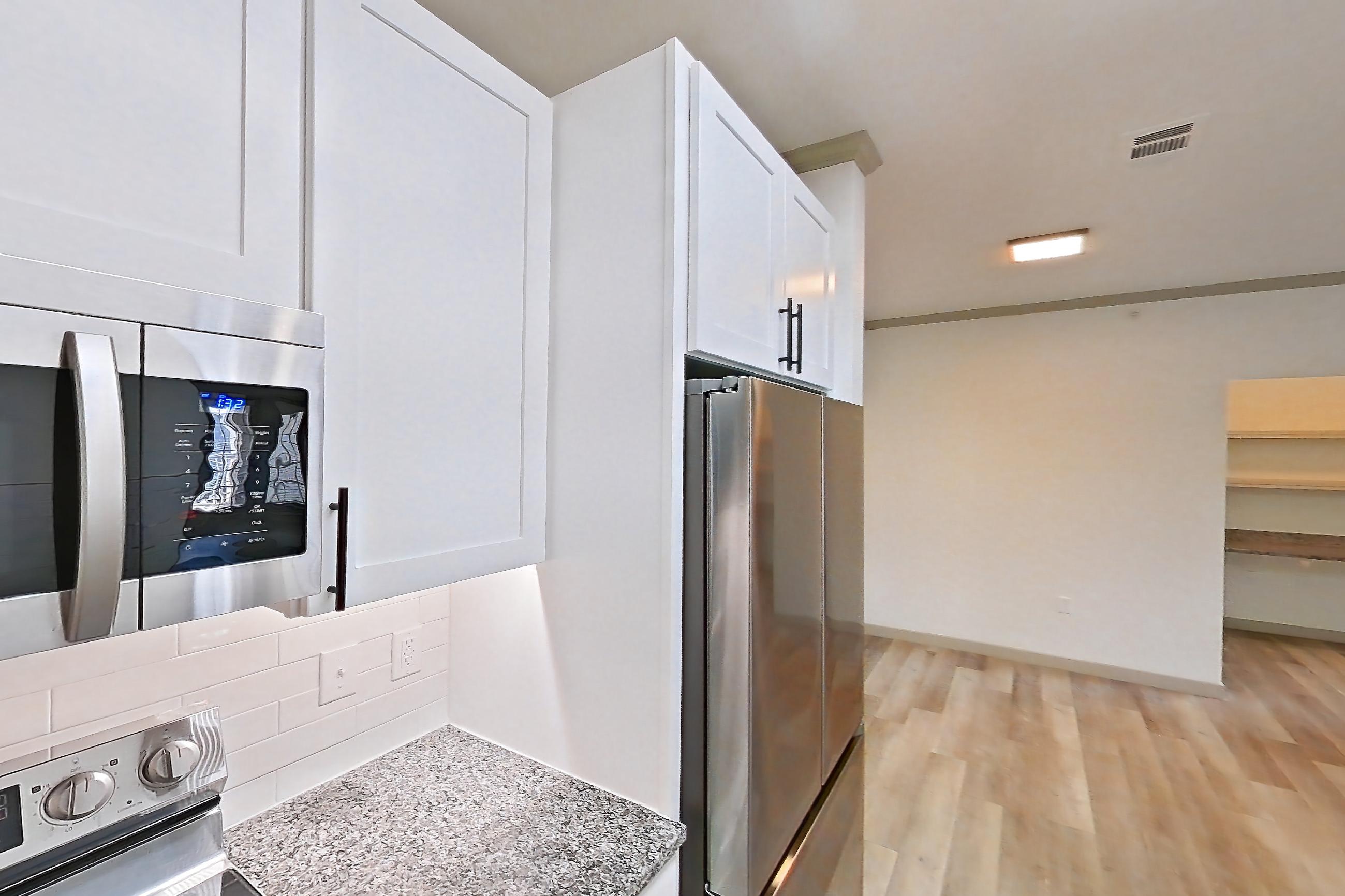 Kitchen with dishwasher, electric range, light countertops, light stone countertops, light wood-finish flooring, microwave, oven/range, refrigerator, and stainless steel appliances, Apartment 04-302 at Cortland Westminster