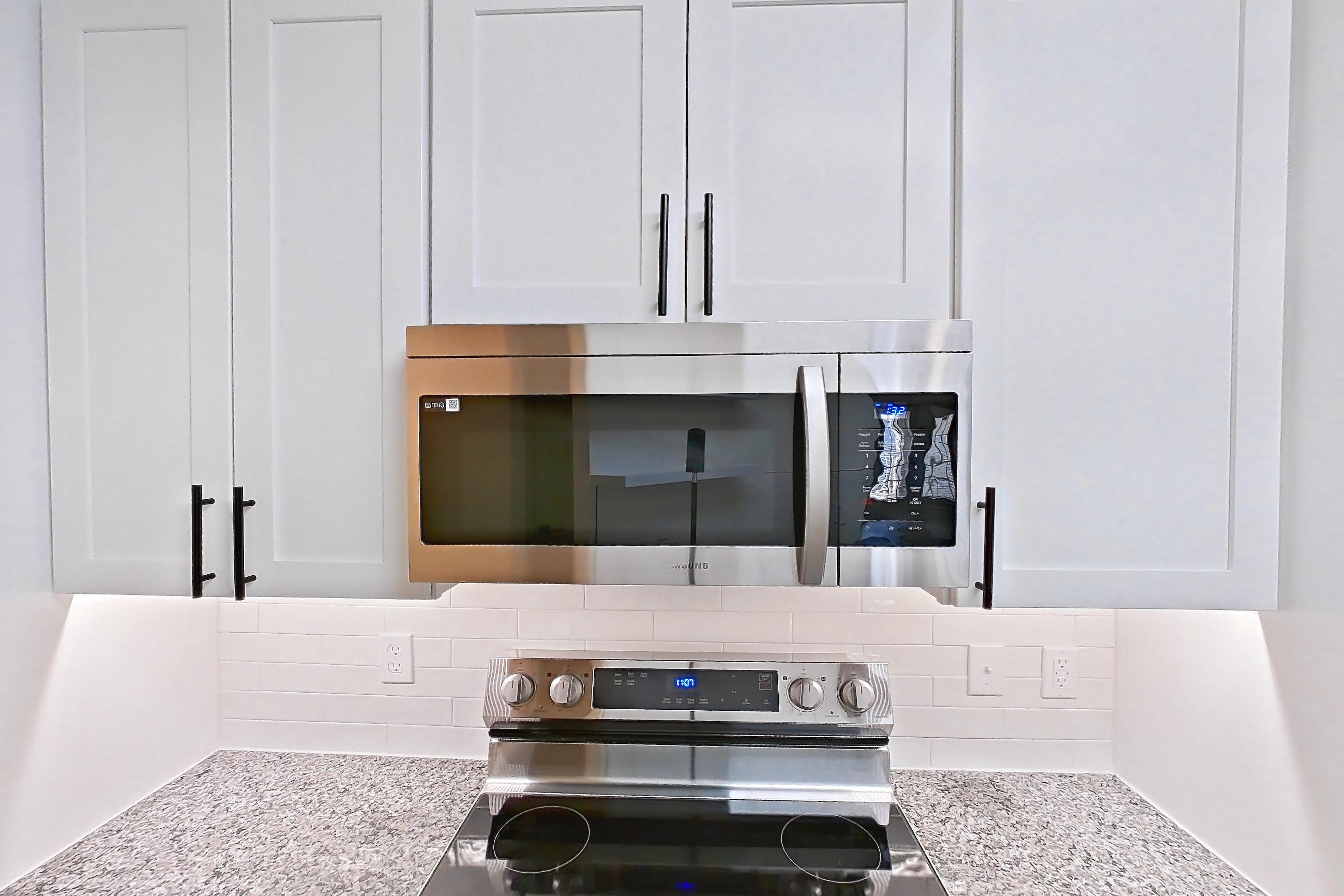Kitchen with dishwasher, electric range, light countertops, light stone countertops, light wood-finish flooring, microwave, oven/range, refrigerator, and stainless steel appliances, Apartment 04-302 at Cortland Westminster