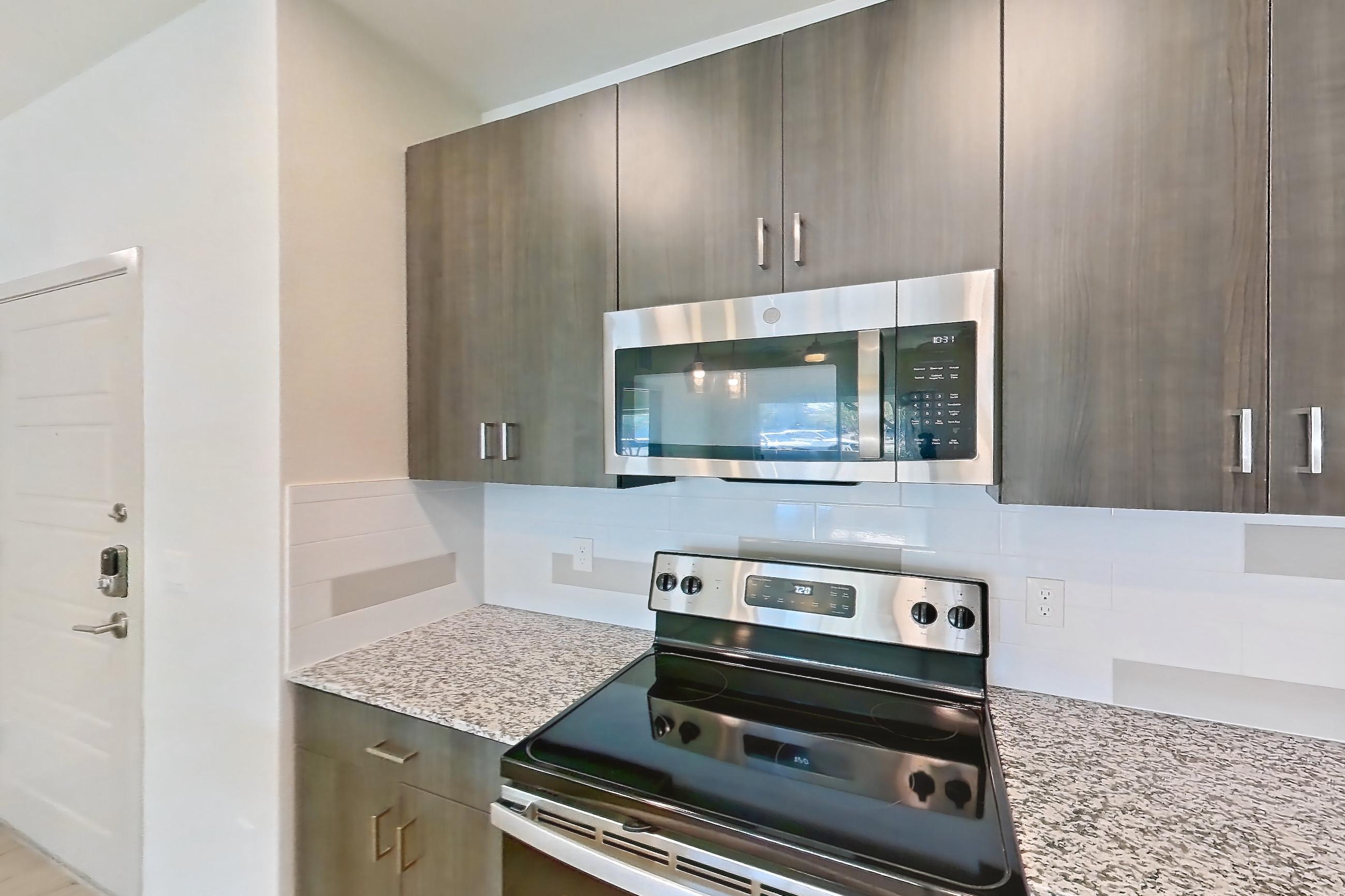 Kitchen with dishwasher, electric range, light stone countertops, light wood-finish flooring, oven/range, refrigerator, and stainless steel appliances, Apartment 1015 at Cortland at P83