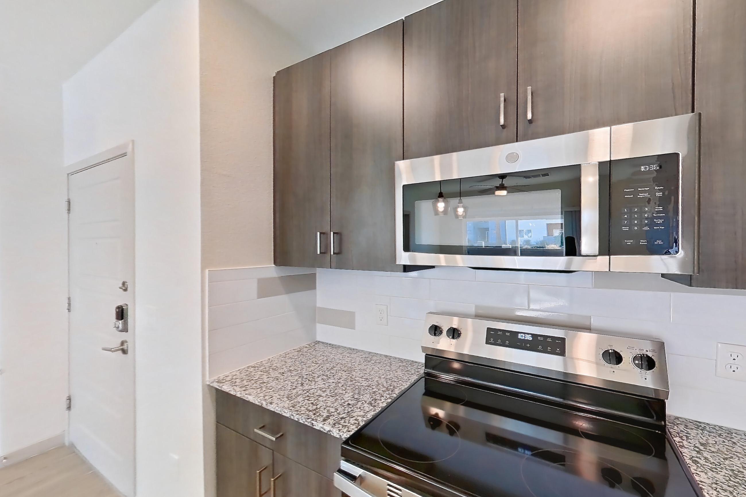 Kitchen with dishwasher, electric range, light stone countertops, light wood-finish flooring, oven/range, refrigerator, and stainless steel appliances, Apartment 1140 at Cortland at P83