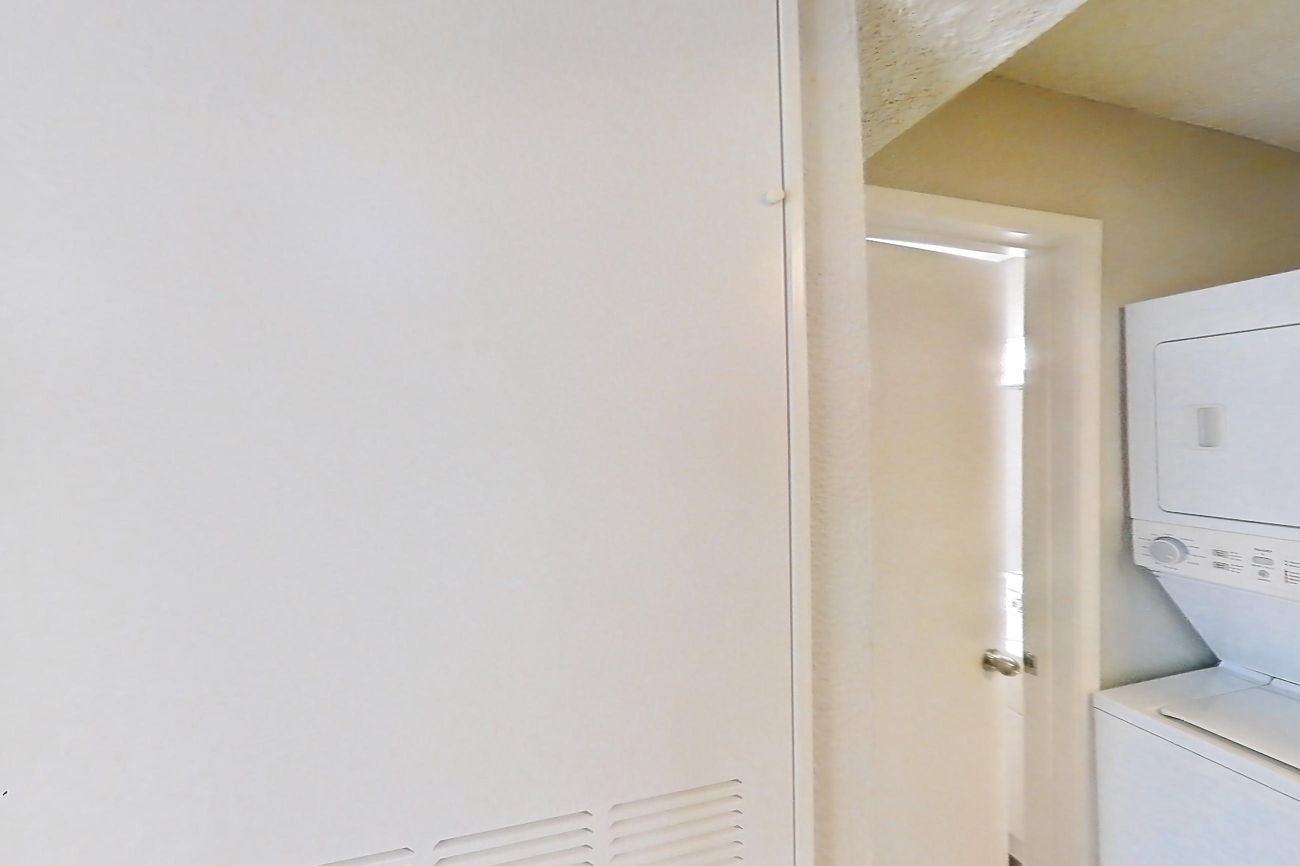 Kitchen entryway with dark wood-finish flooring, dishwasher, electric range, in-unit laundry, light countertops, light stone countertops, light wood-finish flooring, oven/range, refrigerator, and stainless steel appliances, Apartment 2305 at Cortland at the Hammocks