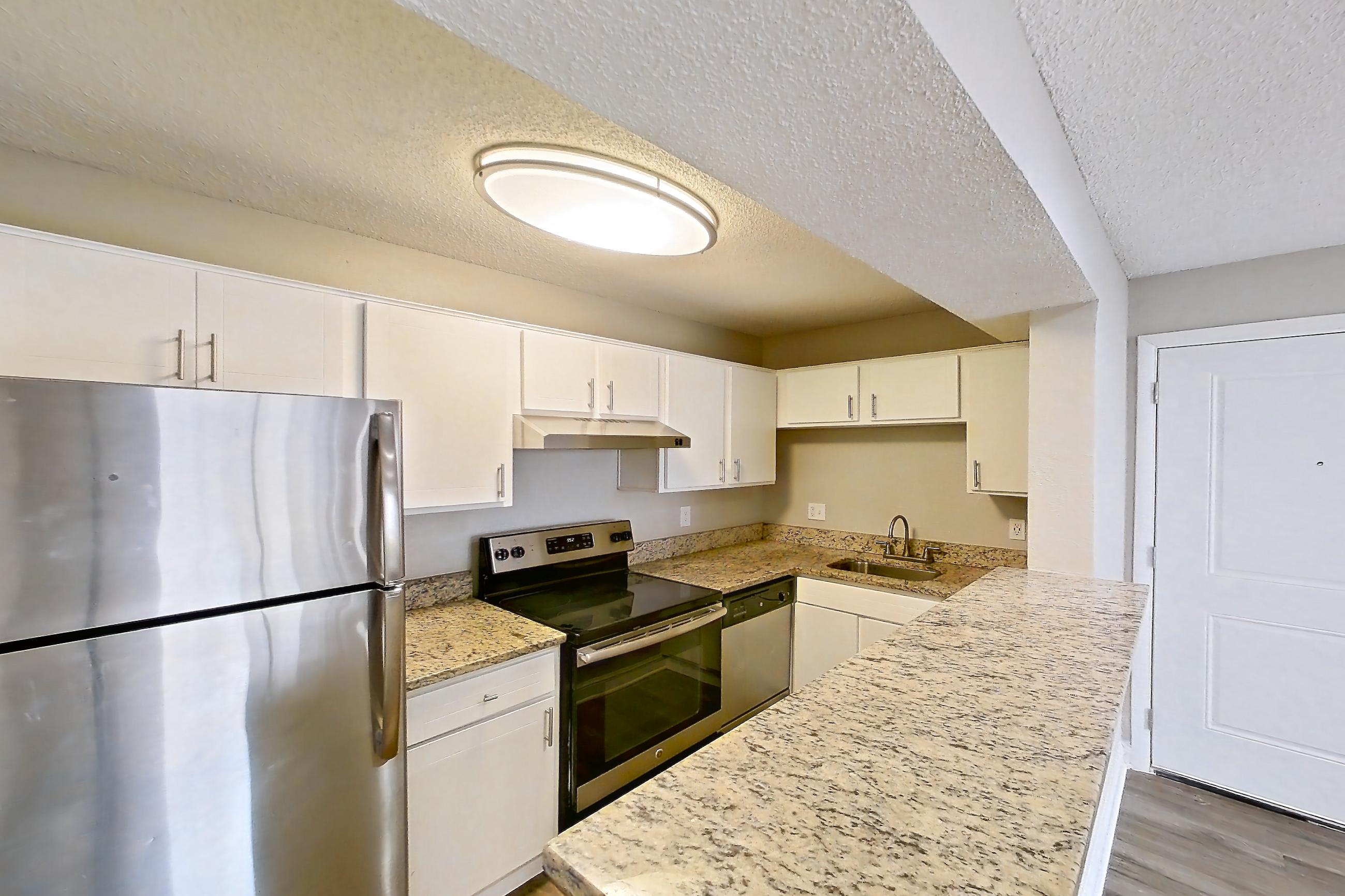 Kitchen entryway with dark wood-finish flooring, dishwasher, electric range, in-unit laundry, light countertops, light stone countertops, light wood-finish flooring, oven/range, refrigerator, and stainless steel appliances, Apartment 2305 at Cortland at the Hammocks