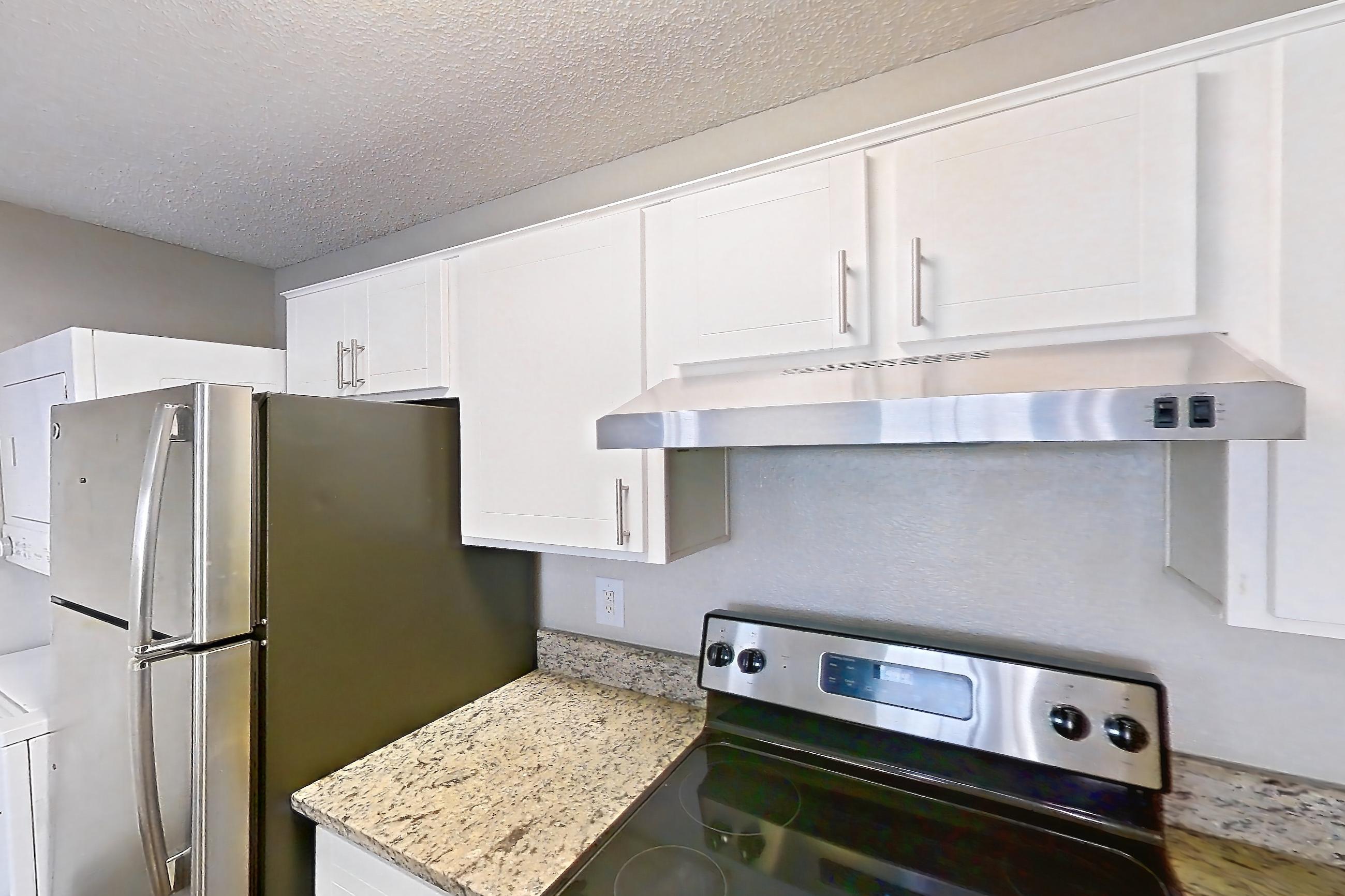 Kitchen with dark wood-finish flooring, dishwasher, electric range, light countertops, light stone countertops, oven/range, refrigerator, and stainless steel appliances, Apartment 2305 at Cortland at the Hammocks