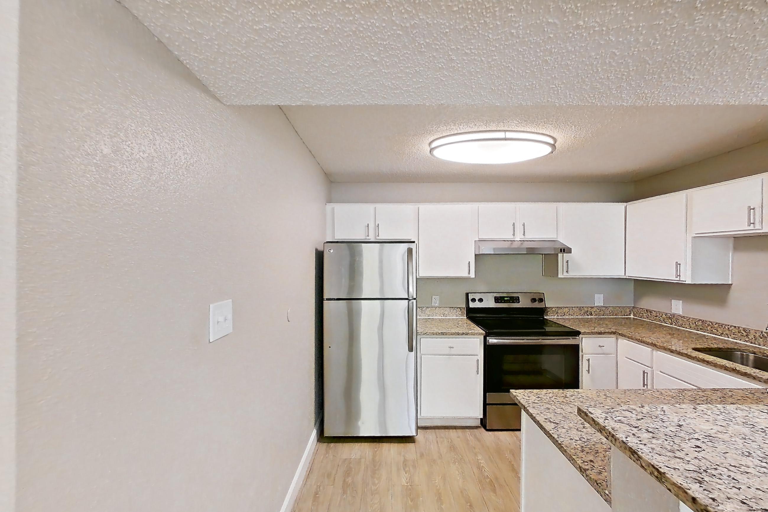 Kitchen entryway with electric range, light carpet, light stone countertops, light wood-finish flooring, oven/range, refrigerator, and stainless steel appliances, Apartment 0506 at Cortland at the Hammocks