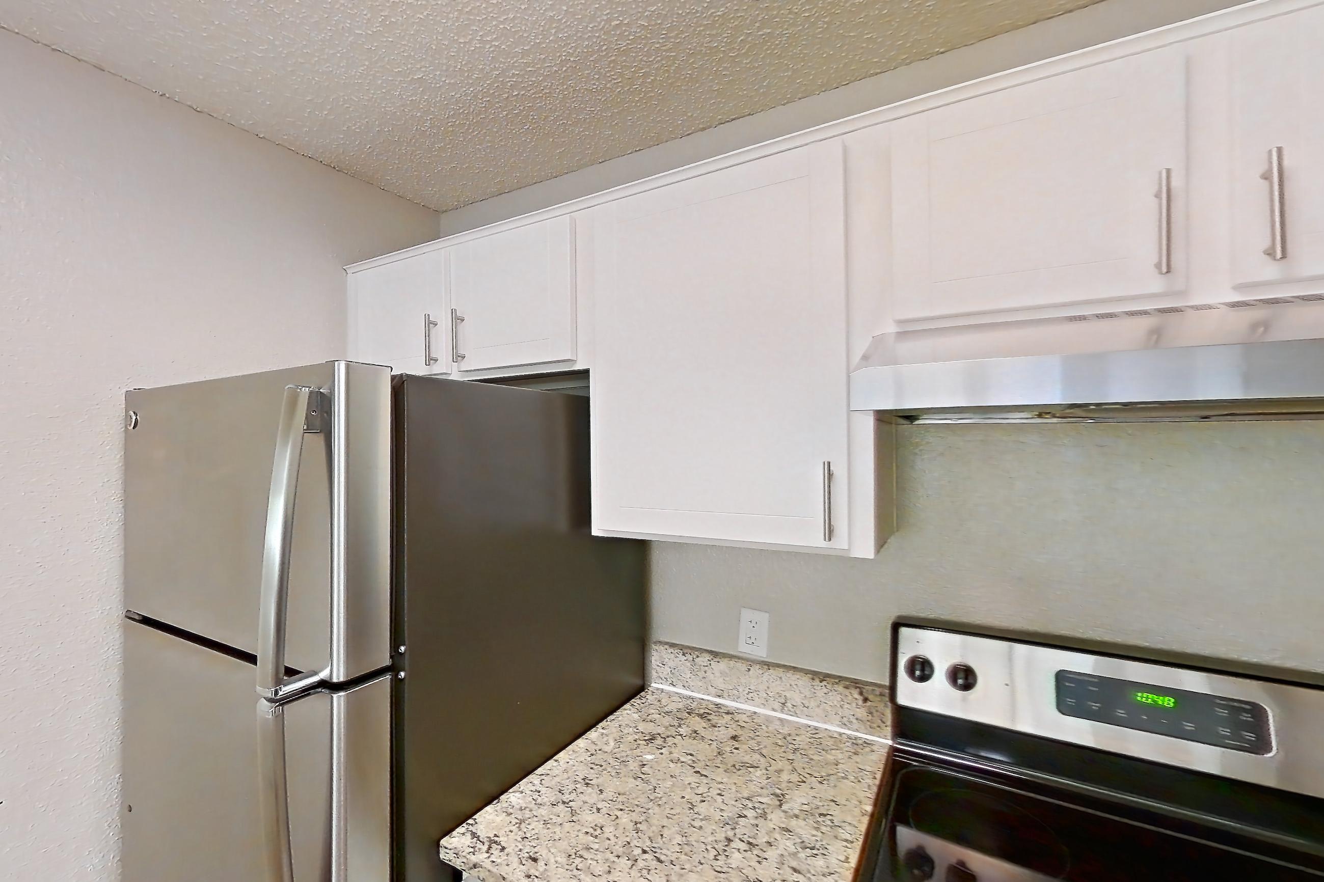 Kitchen with dishwasher, electric range, light carpet, light stone countertops, light wood-finish flooring, oven/range, range hood, refrigerator, and stainless steel appliances, Apartment 0506 at Cortland at the Hammocks