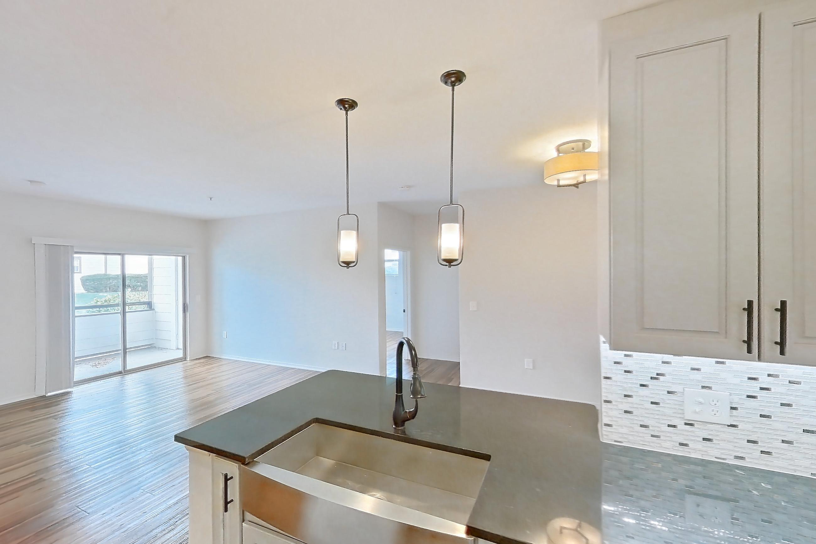 Kitchen with black appliances, dark countertops, dark stone countertops, dishwasher, electric range, light countertops, light wood-finish flooring, microwave, oven/range, and stainless steel appliances, Apartment 1418 at Cortland Grand River