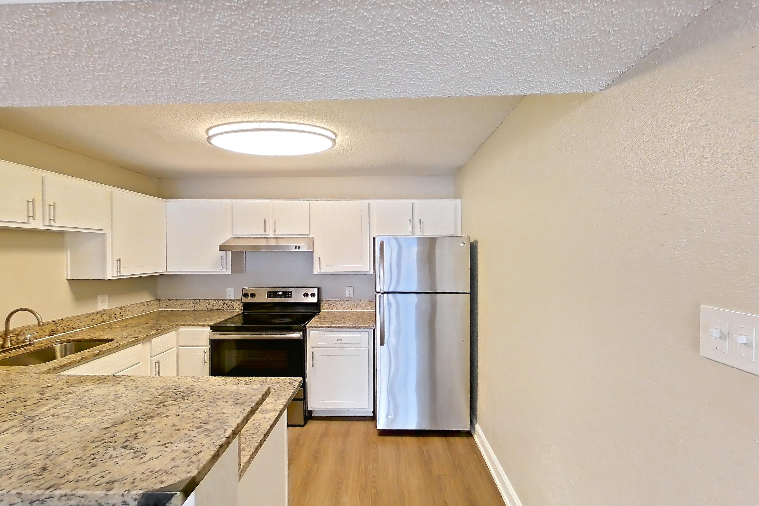 Kitchen entryway with dark wood-finish flooring, electric range, light countertops, light stone countertops, light wood-finish flooring, oven/range, refrigerator, and stainless steel appliances, Apartment 2421 at Cortland at the Hammocks