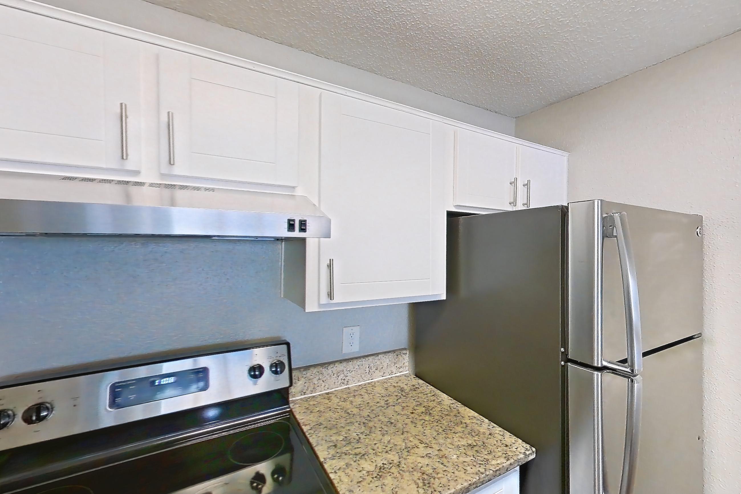 Kitchen with dark wood-finish flooring, dishwasher, electric range, light stone countertops, light wood-finish flooring, oven/range, range hood, refrigerator, and stainless steel appliances, Apartment 2421 at Cortland at the Hammocks