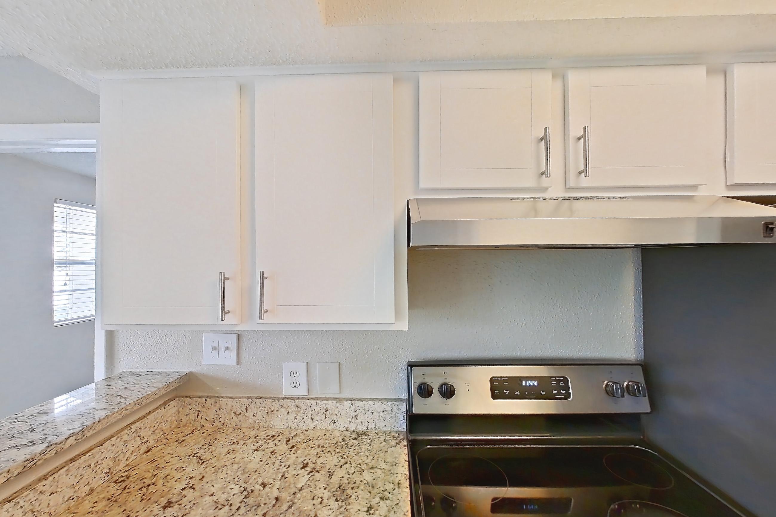 Kitchen with dishwasher, electric range, light carpet, light countertops, light stone countertops, light wood-finish flooring, oven/range, refrigerator, and stainless steel appliances, Apartment 1710 at Cortland at the Hammocks