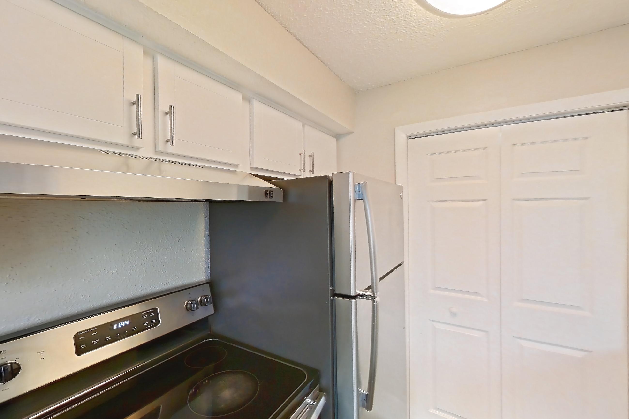 Kitchen with dishwasher, electric range, light carpet, light countertops, light stone countertops, light wood-finish flooring, oven/range, refrigerator, and stainless steel appliances, Apartment 1710 at Cortland at the Hammocks