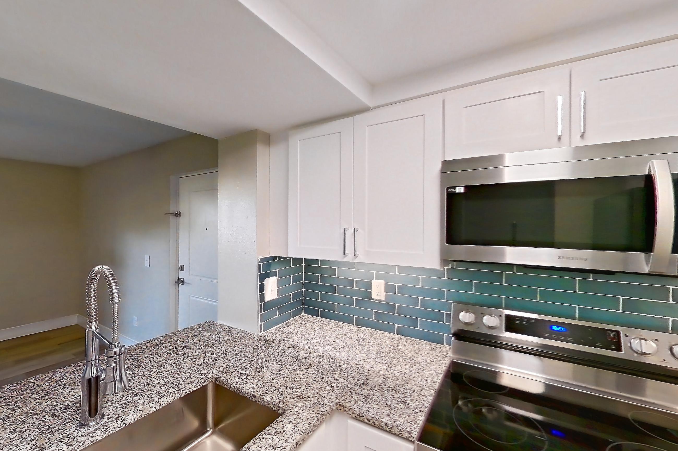 Kitchen with dishwasher, electric range, light countertops, light stone countertops, light wood-finish flooring, microwave, oven/range, refrigerator, and stainless steel appliances, Apartment 01-017 at Cortland at the Hammocks