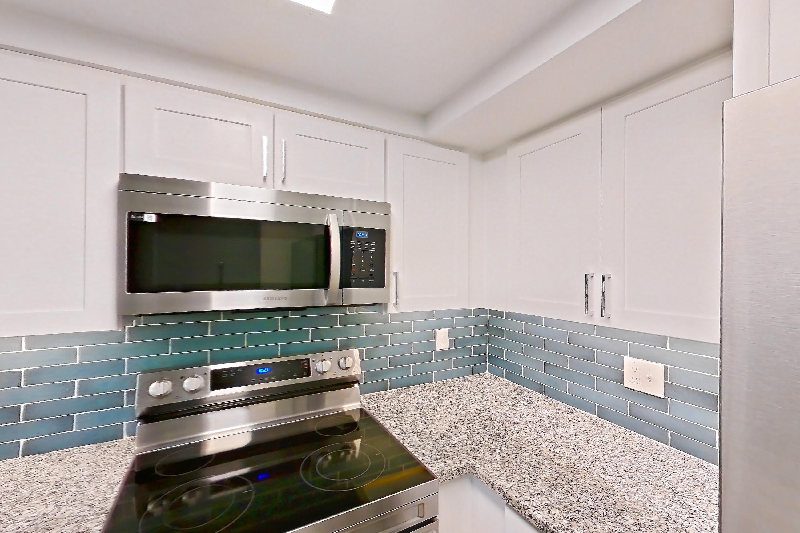 Kitchen with dishwasher, electric range, light countertops, light stone countertops, light wood-finish flooring, microwave, oven/range, refrigerator, and stainless steel appliances, Apartment 01-017 at Cortland at the Hammocks