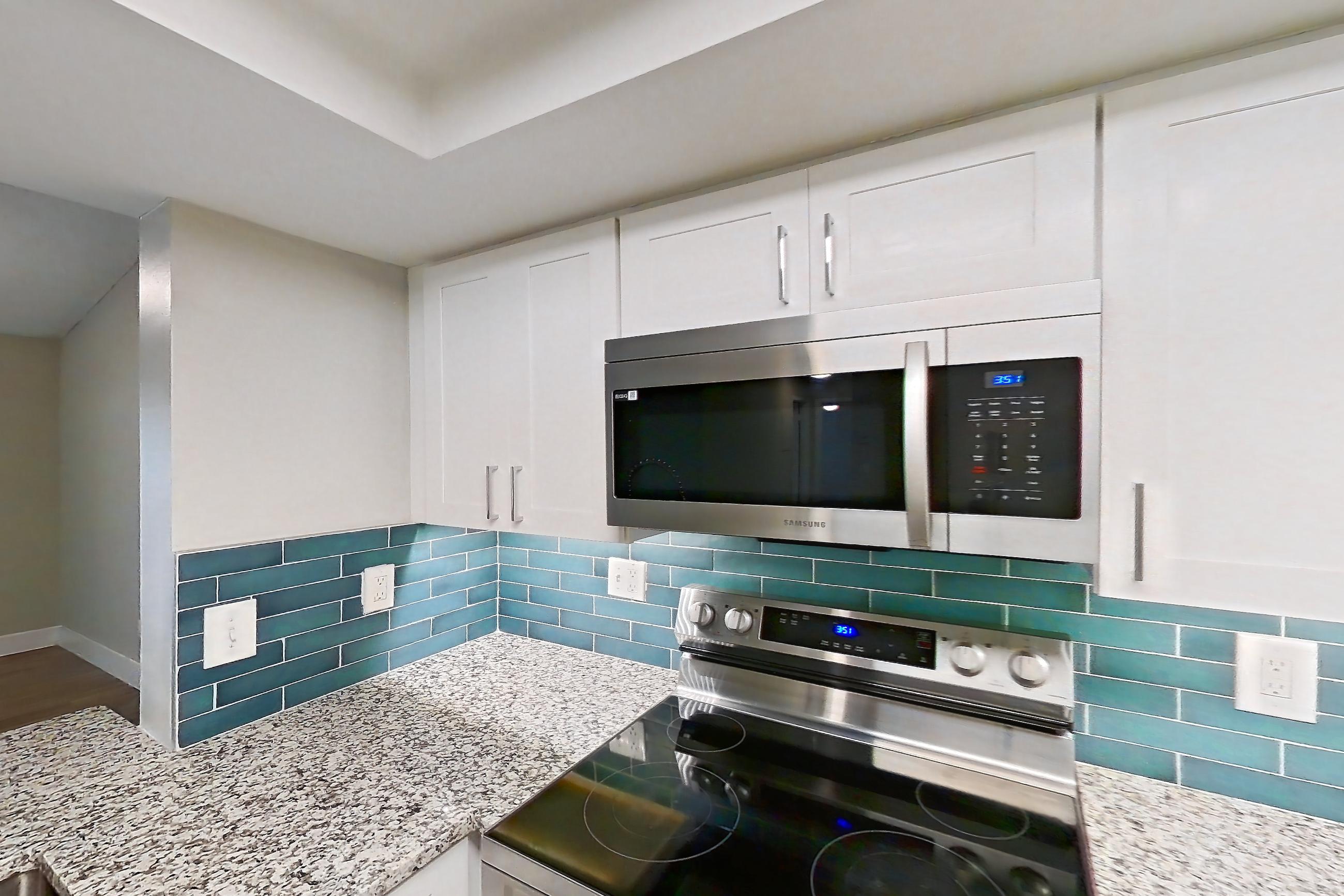 Kitchen with electric range, light countertops, light stone countertops, light wood-finish flooring, microwave, oven/range, and stainless steel appliances, Apartment 02-037 at Cortland at the Hammocks