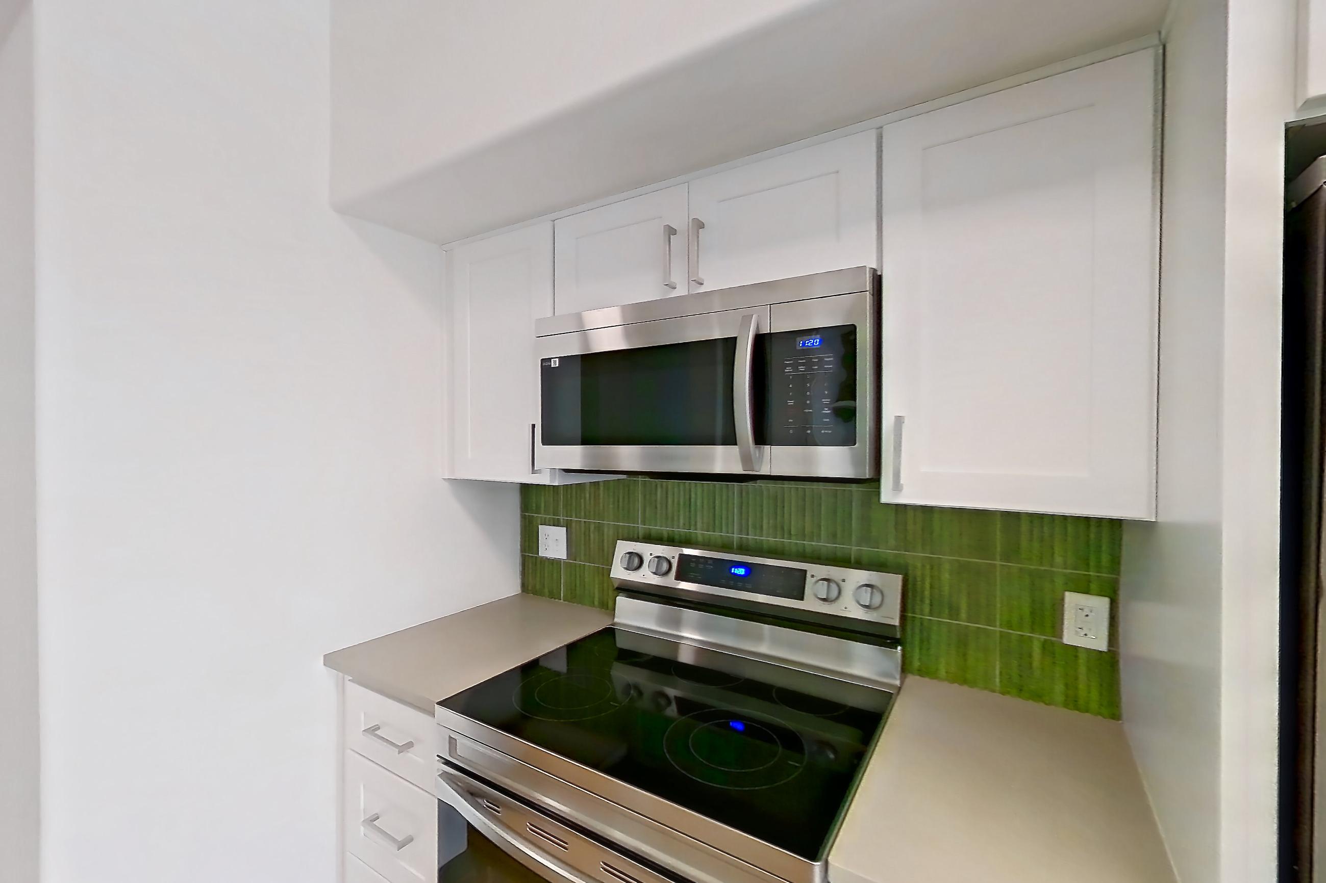Kitchen with dishwasher, electric range, light countertops, light stone countertops, light wood-finish flooring, microwave, oven/range, refrigerator, and stainless steel appliances, Apartment 12309 at Cortland Lakecrest